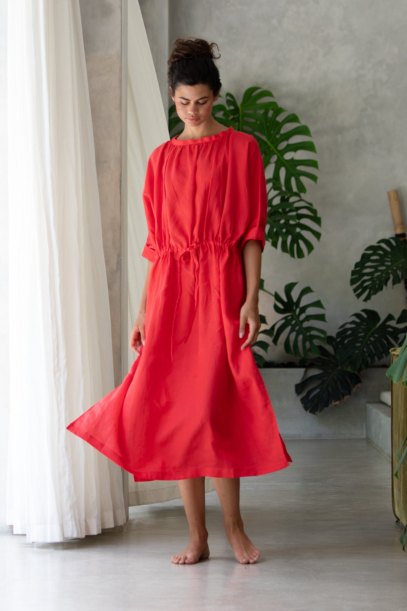 flowing red linen dress with the beautiful model looking down at the ground  