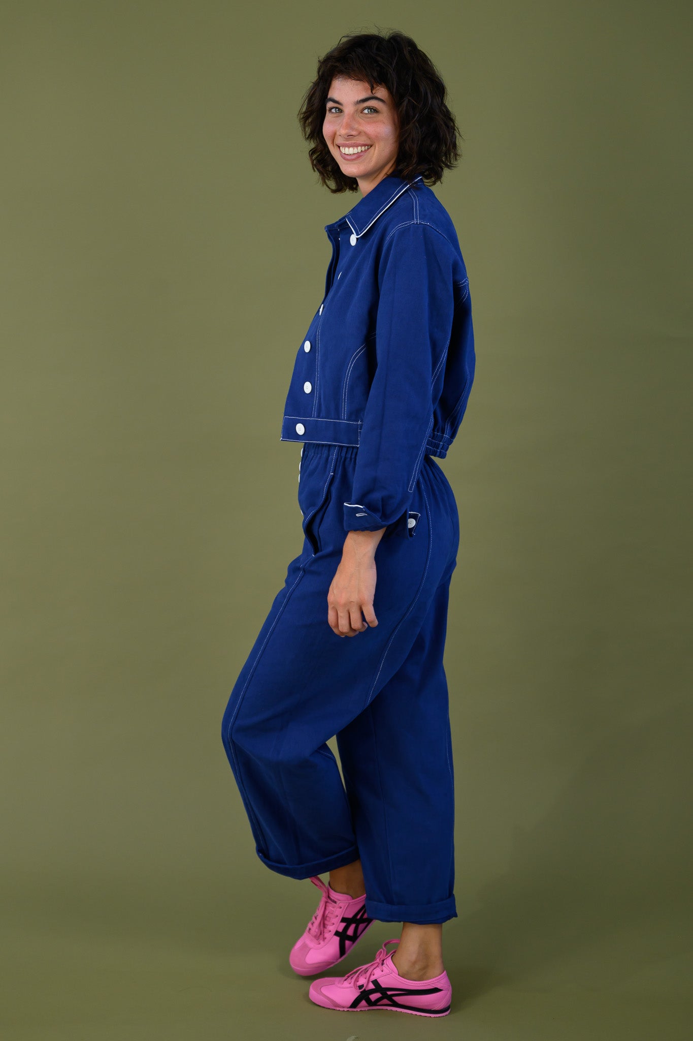 Side profile of blue cotton twill cropped jacket with white buttons and elasticated waist