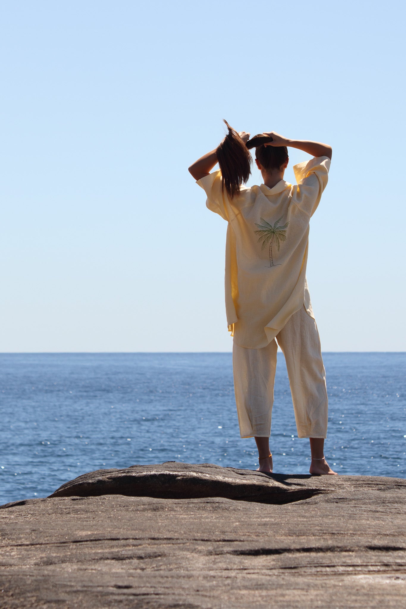 Back view of the Salt Pant in butter yellow paired with embroidered palm shirt, highlighting relaxed cropped hem and coastal styling.