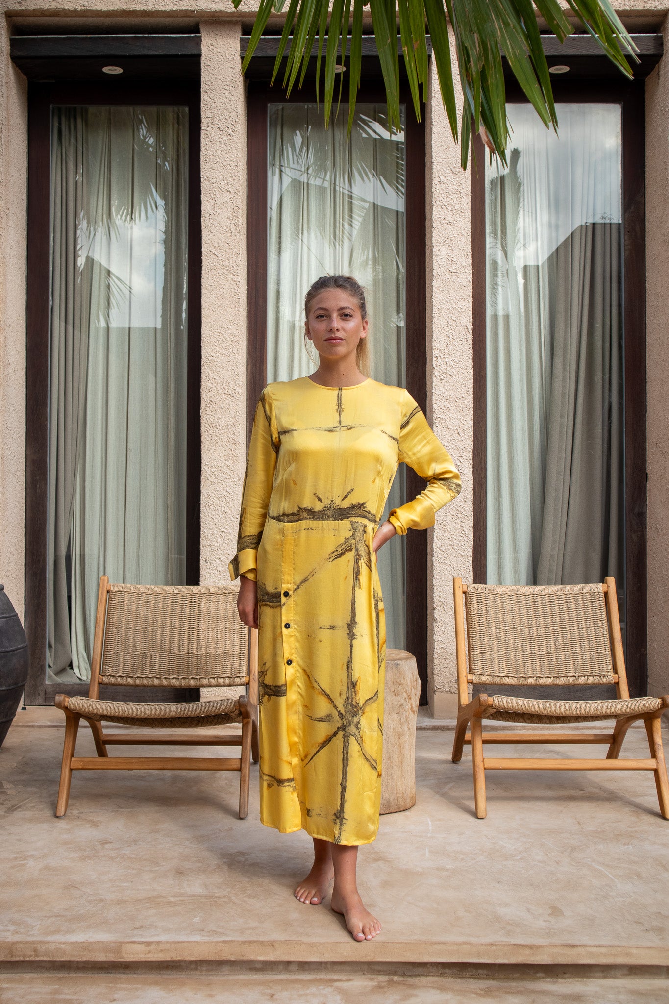 Front view of model in the Maggie Dress in mango Shibori with relaxed elegance and earthy backdrop.