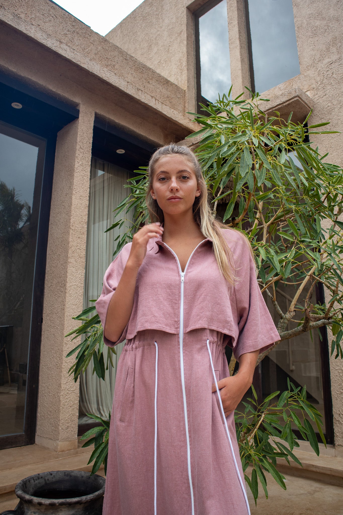 Model wearing dusty pink Iconica dress with white zip front and cropped overlay from The Boy and I's Japandi collection