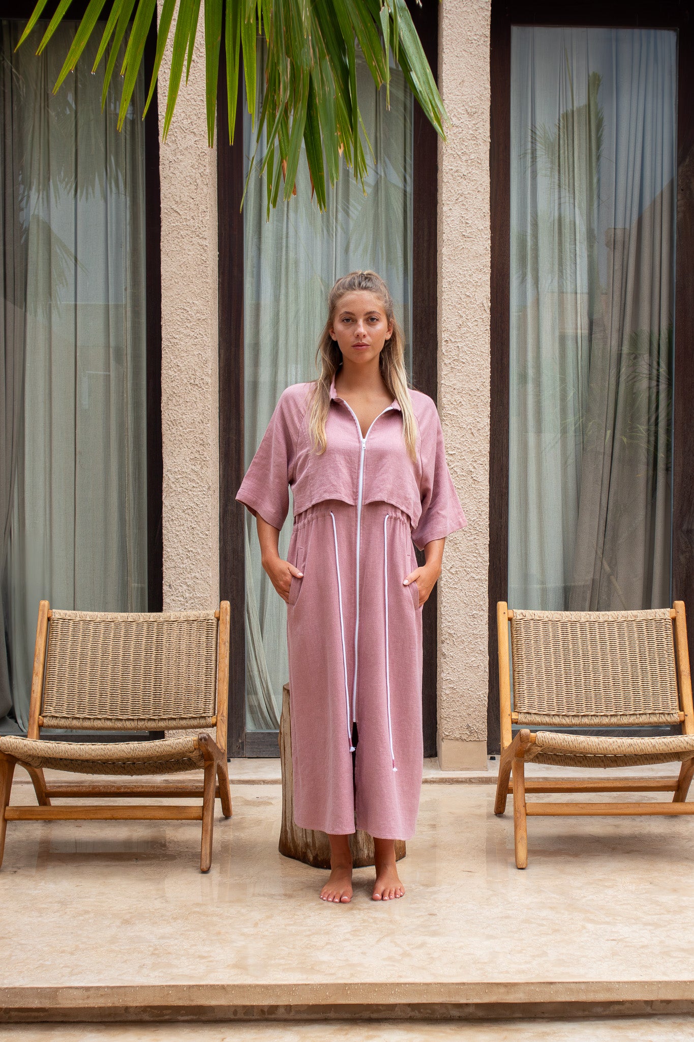 Model wearing dusty pink Iconica dress from The Boy and I, styled in front of tropical modern house with palm leaves above