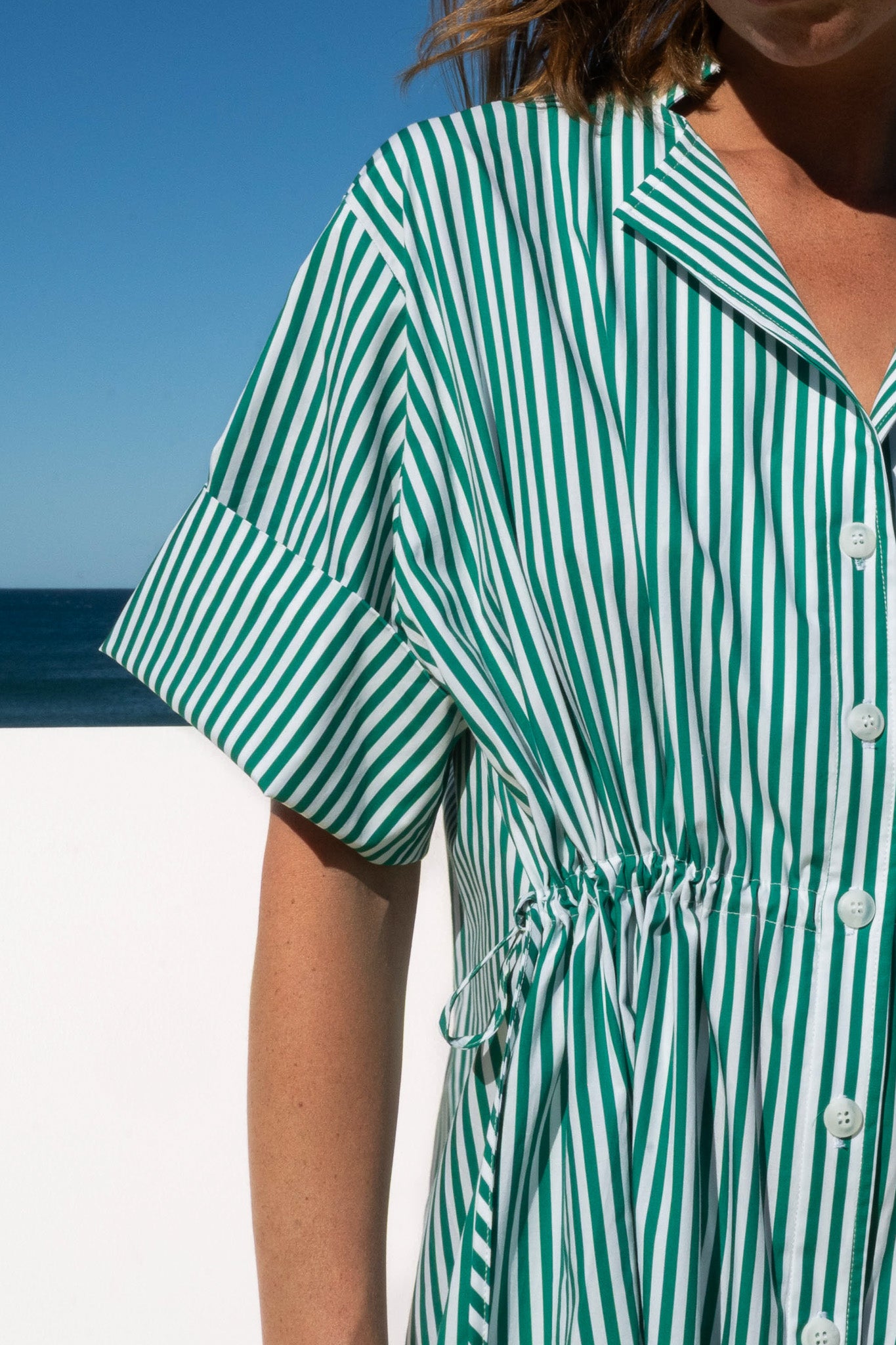Close-up of the Leon Dress in lush green meadow stripe cotton, highlighting the cuffed sleeve and adjustable drawstring waist.