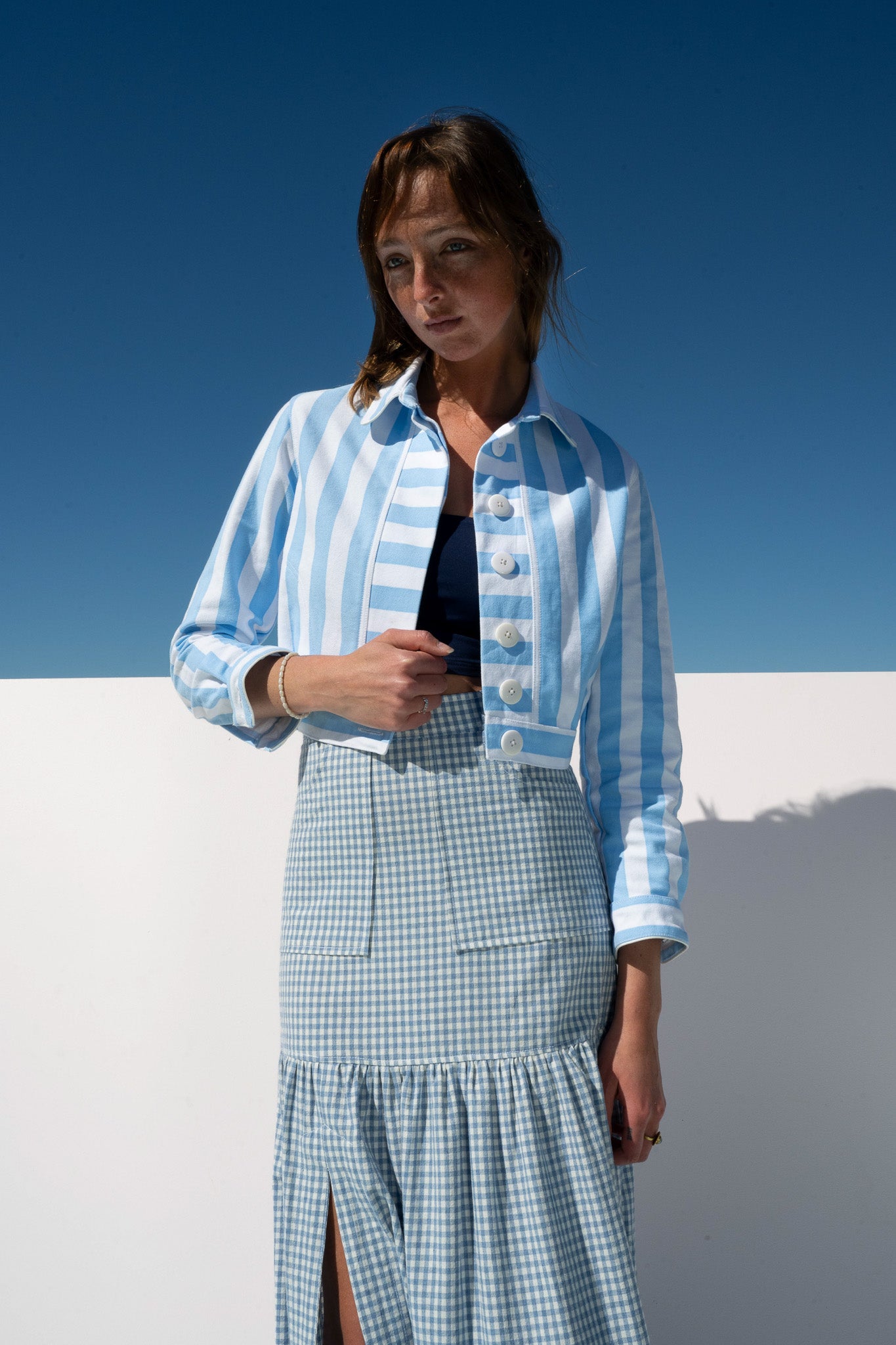 Mon Petit Jacket Saltwater Stripe styled with gingham skirt, angled shot against ocean sky.