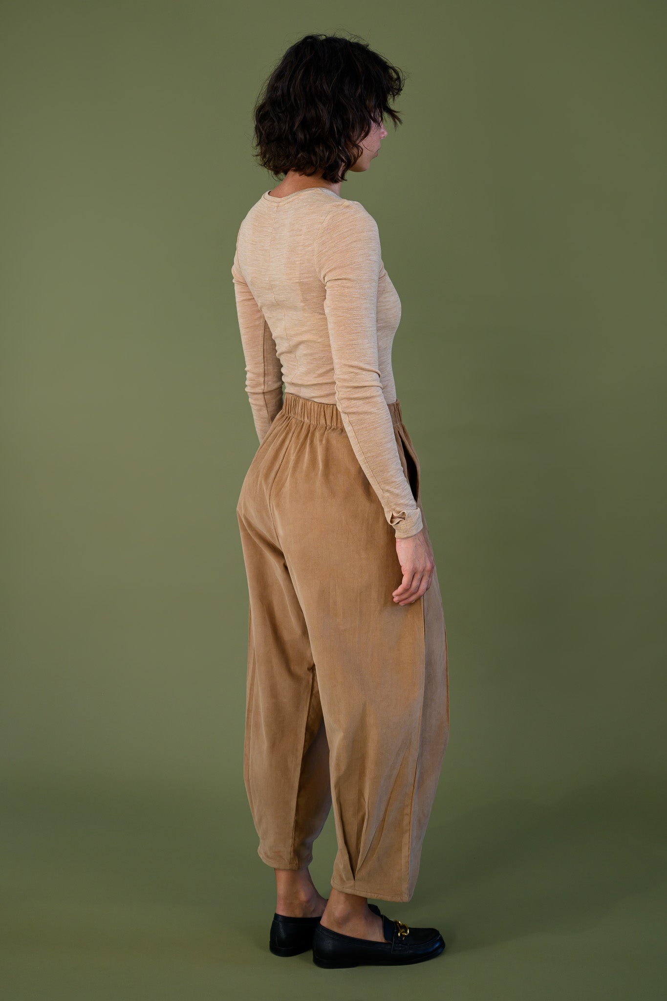 Salt pant in tawny brown cotton corduroy back angled view with neutral long sleeve top showing relaxed fit and tapered leg