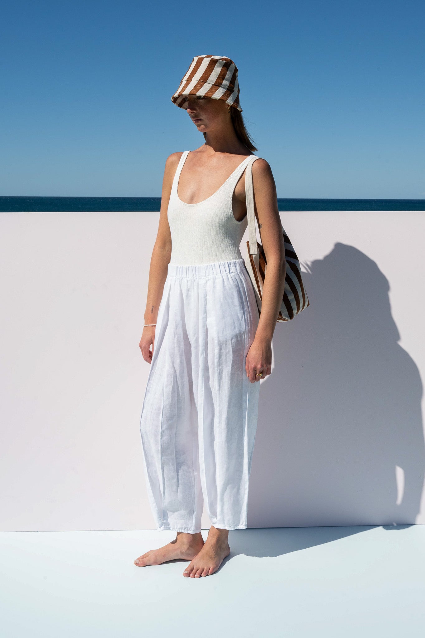 Side view of Salt Pants in white linen styled with white tank and striped accessories.