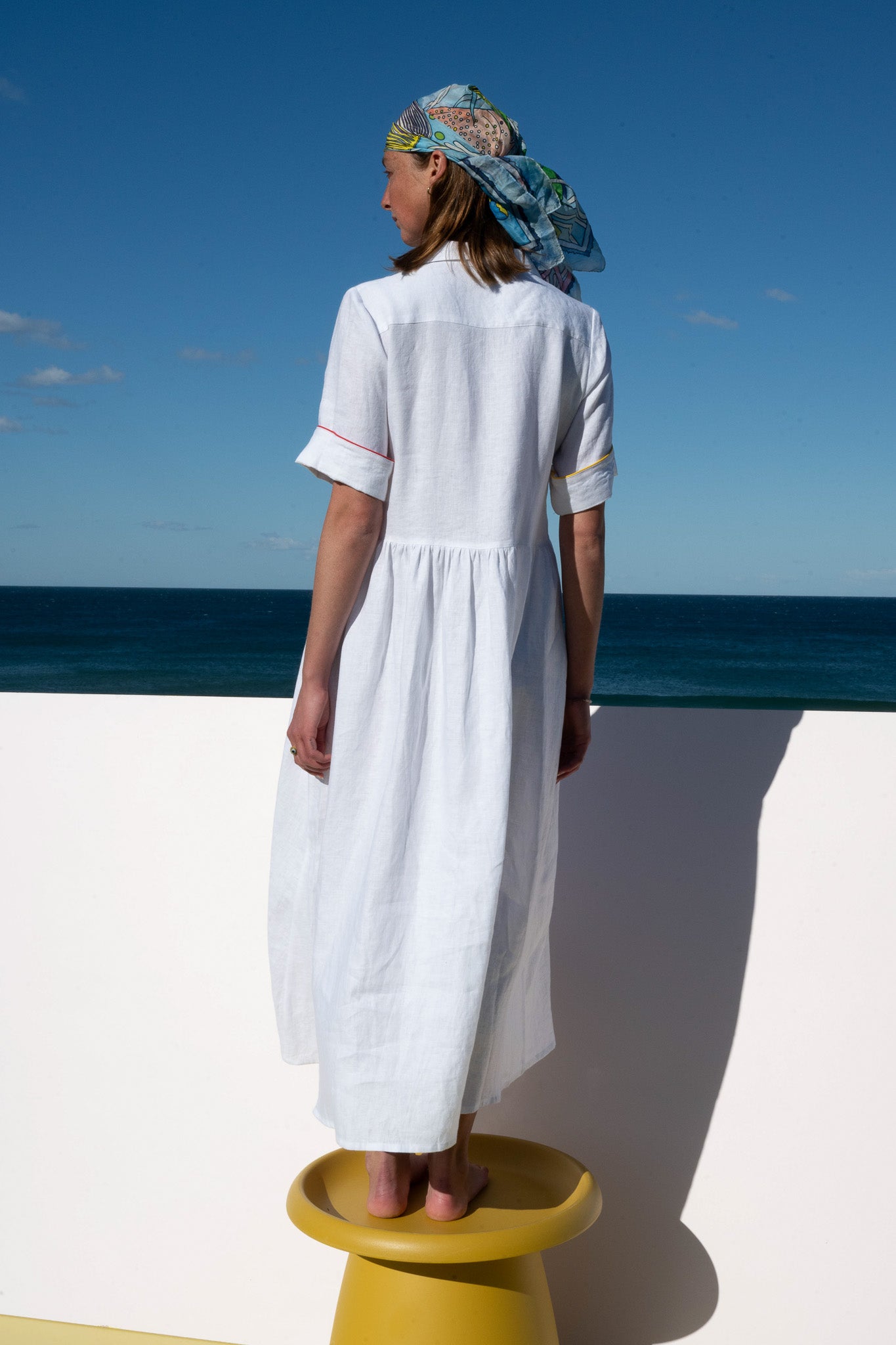 Back view of the Siena Dress in breathable white linen with contrast piping detail