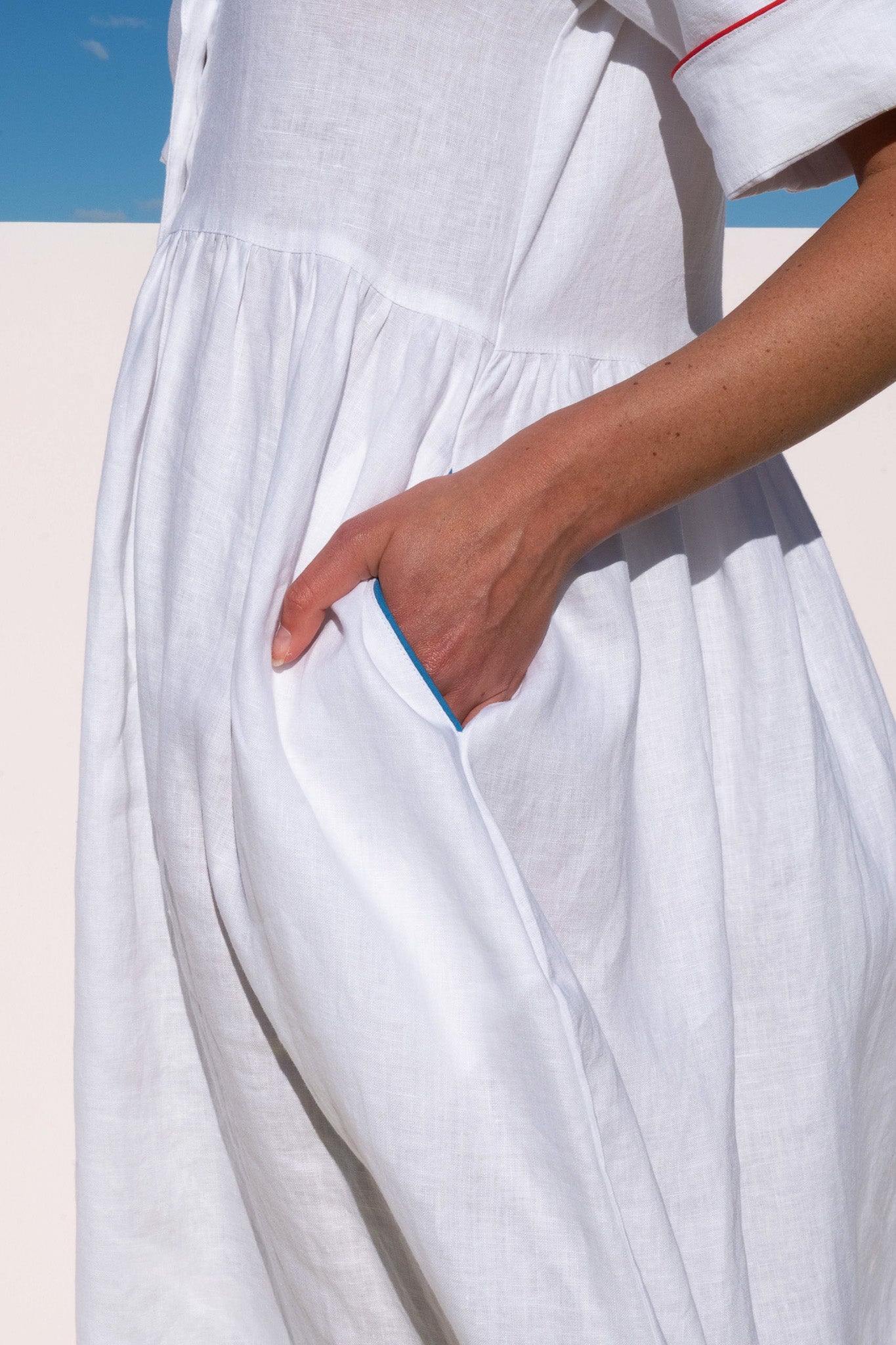 Close-up of Siena Dress in white linen showing side pocket with blue piping detail