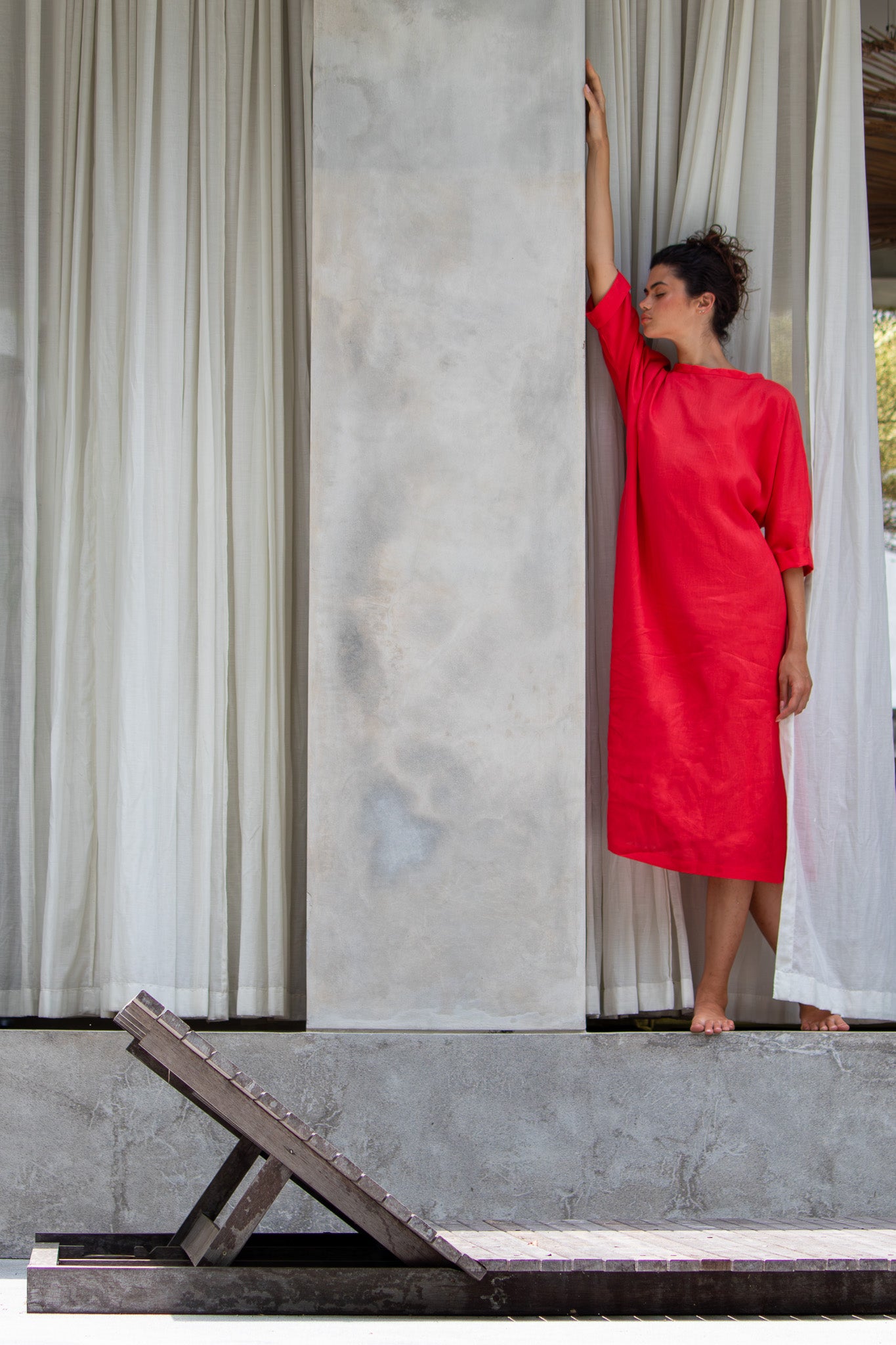 Model Striking stunning pose leaning up against the wall in red linen dress