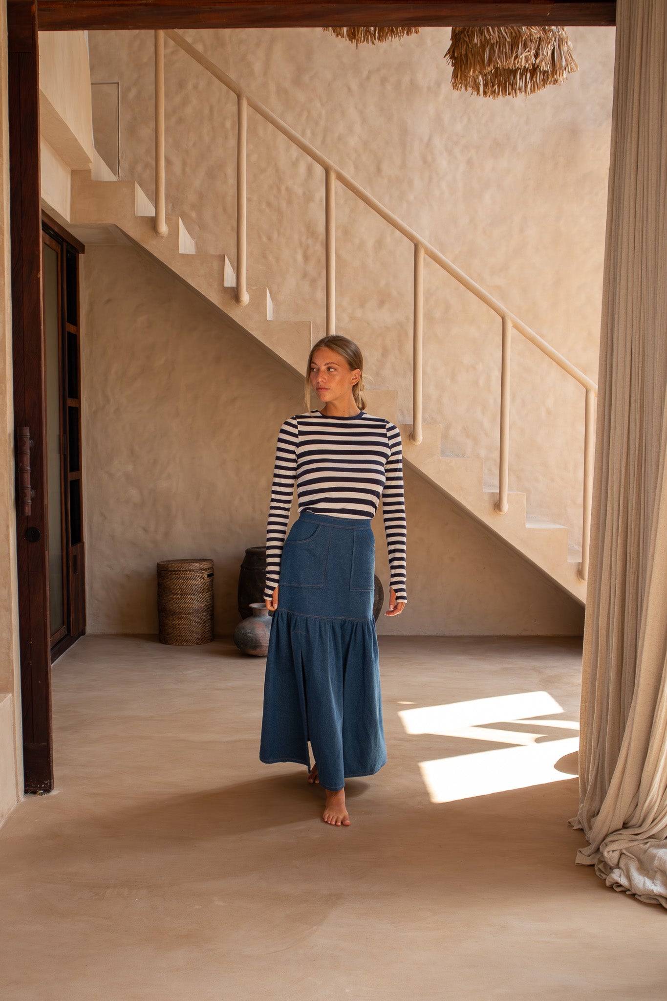Woman walking indoors in The Boy and I Cancan Skirt in denim, captured mid-stride under a softly lit staircase.