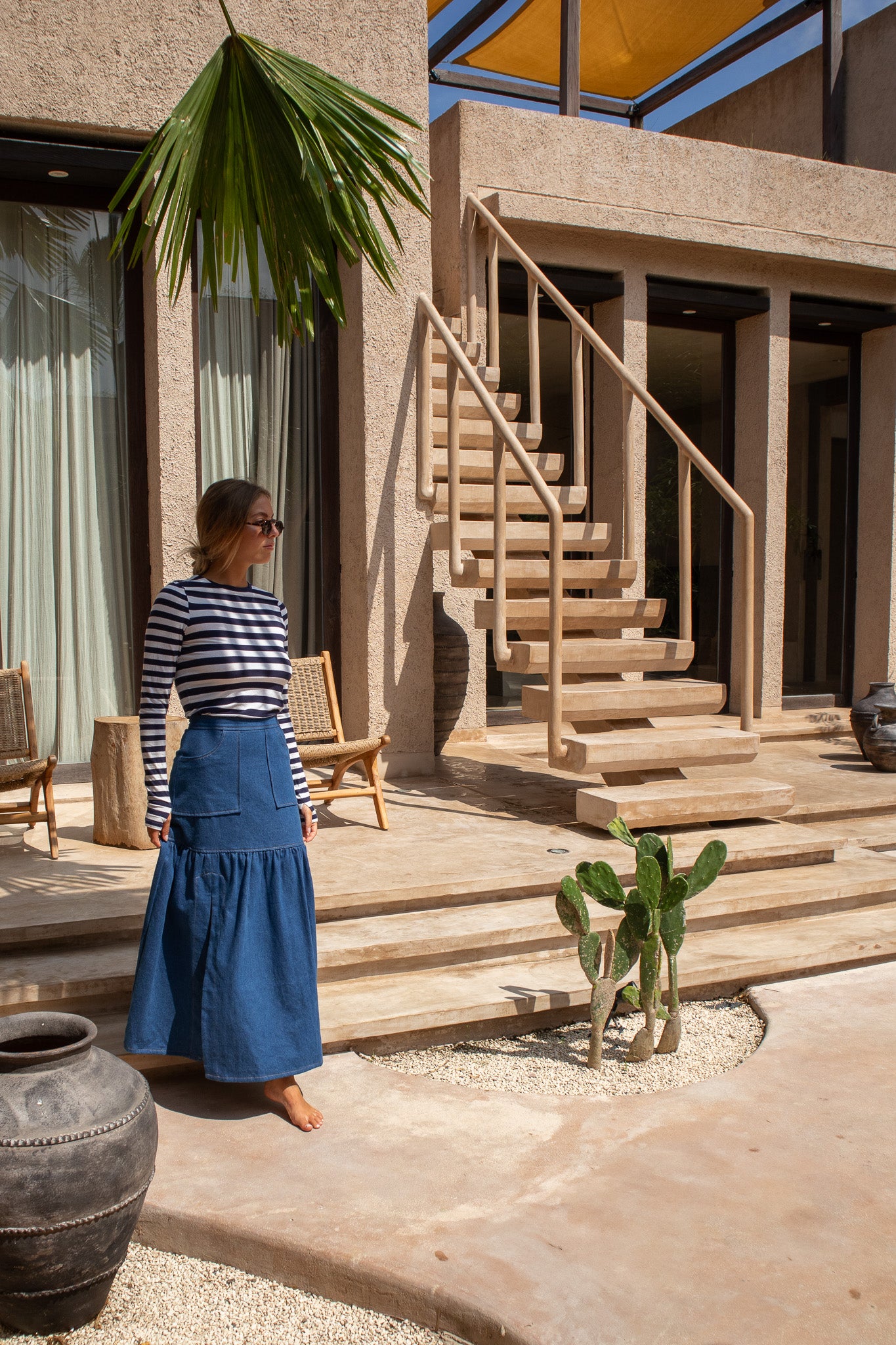Woman walking indoors in The Boy and I Cancan Skirt in denim, captured mid-stride under a softly lit staircase.