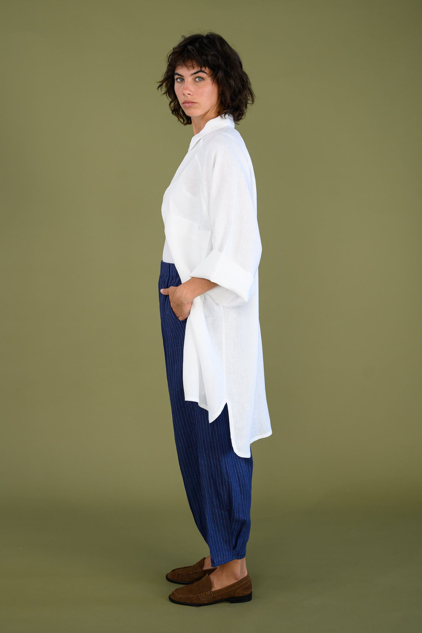 Side profile of white linen shirt dress styled with blue pants