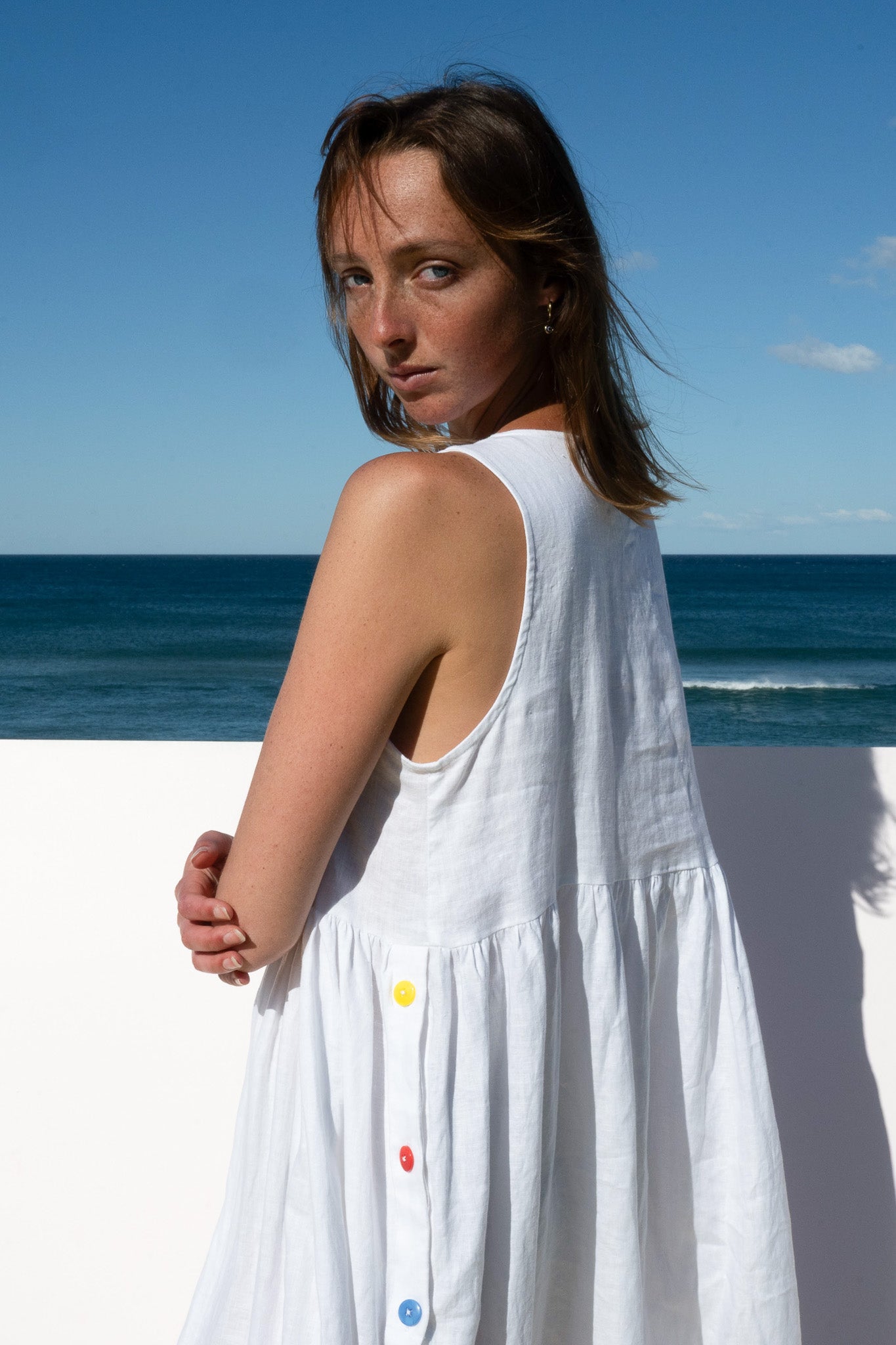 Side close-up of the Wonka Sleeveless Dress in white linen featuring colorful rainbow buttons.