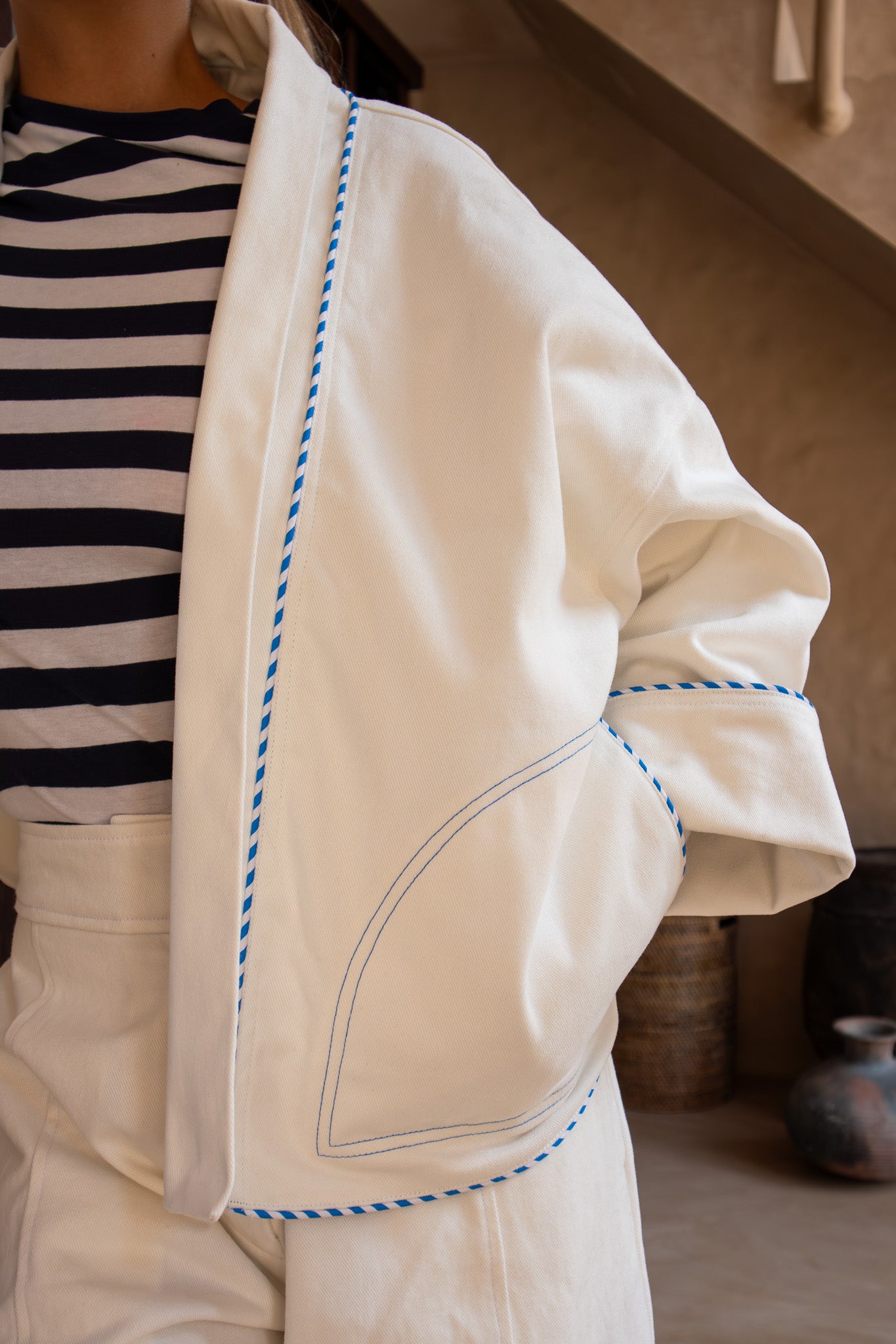 Close-up of the Yoko Kimono Shortie in vanilla showing contrast piping and curved pocket detail, styled with high-waisted wide-leg pants.