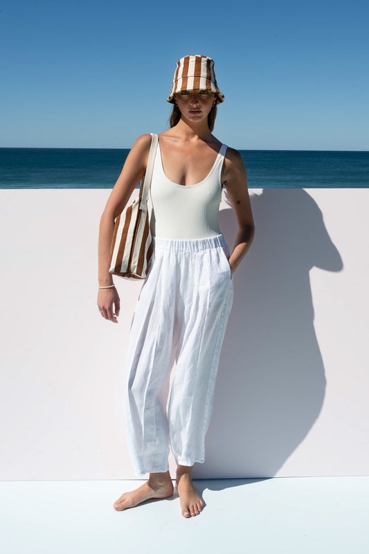 Model wearing bucket hat and bucket bag in caramel stripe with beach back drop 