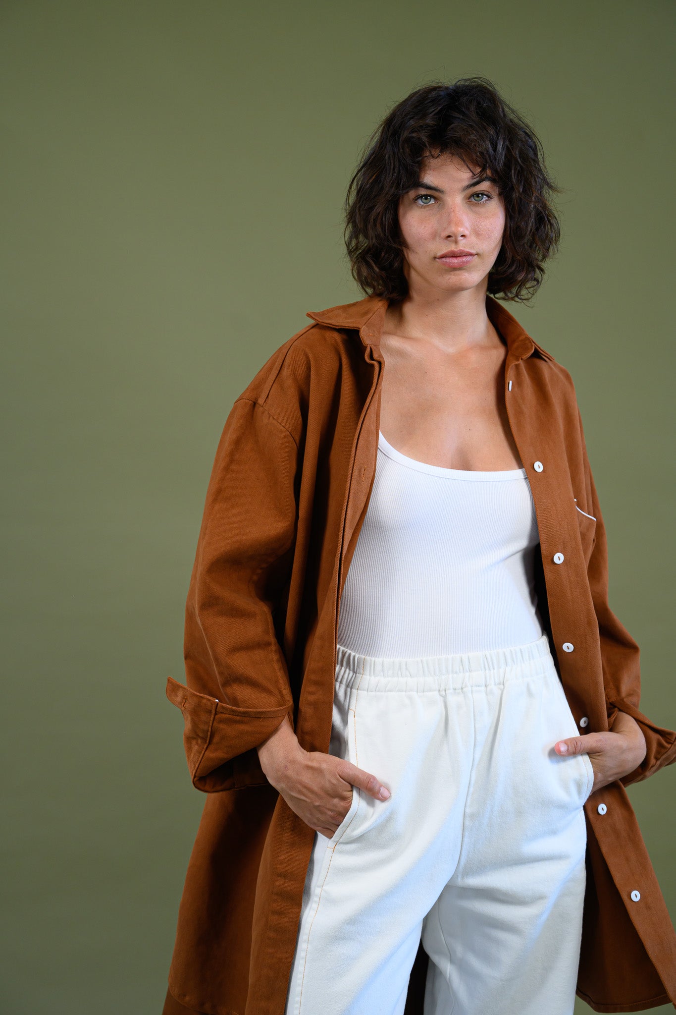 Front portrait view of Caramel cotton canvas denim shirt coat worn open over white outfit with hands in pockets