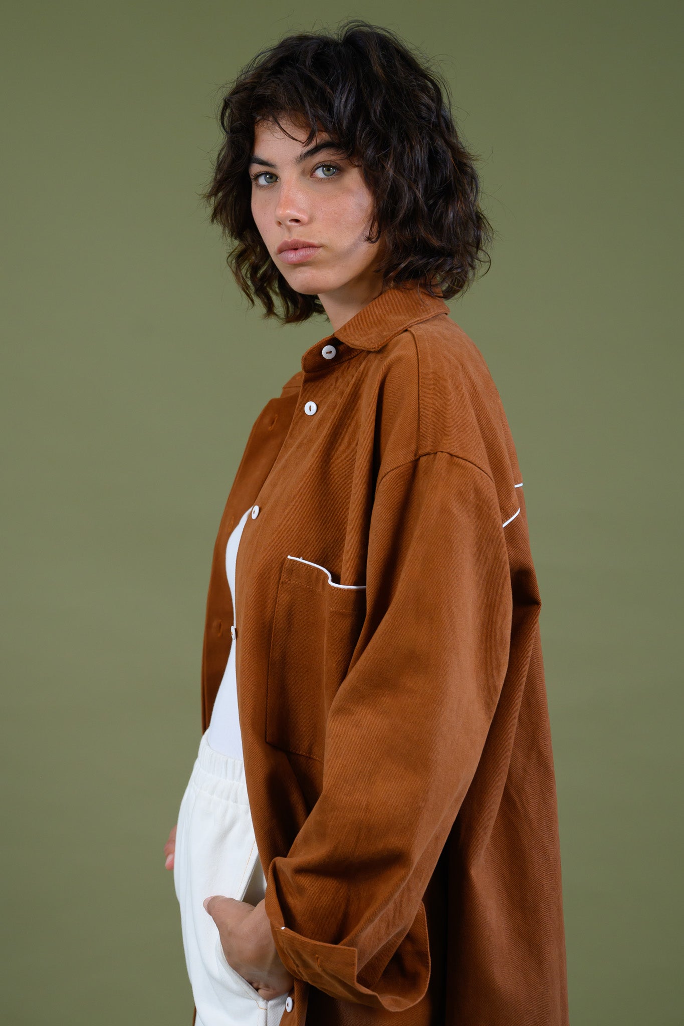 Side portrait view of rCaramel cotton canvas denim shirt coat worn open over white outfit