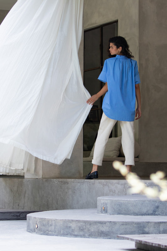 back image of blue cotton poplin blouse shirt, Model holding curtain