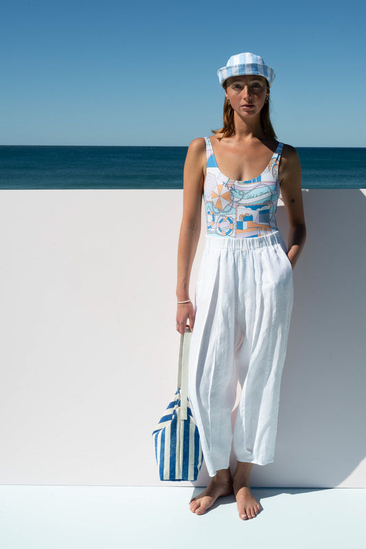Salt Pants in white linen styled with blue printed swimsuit and blue striped bucket hat.