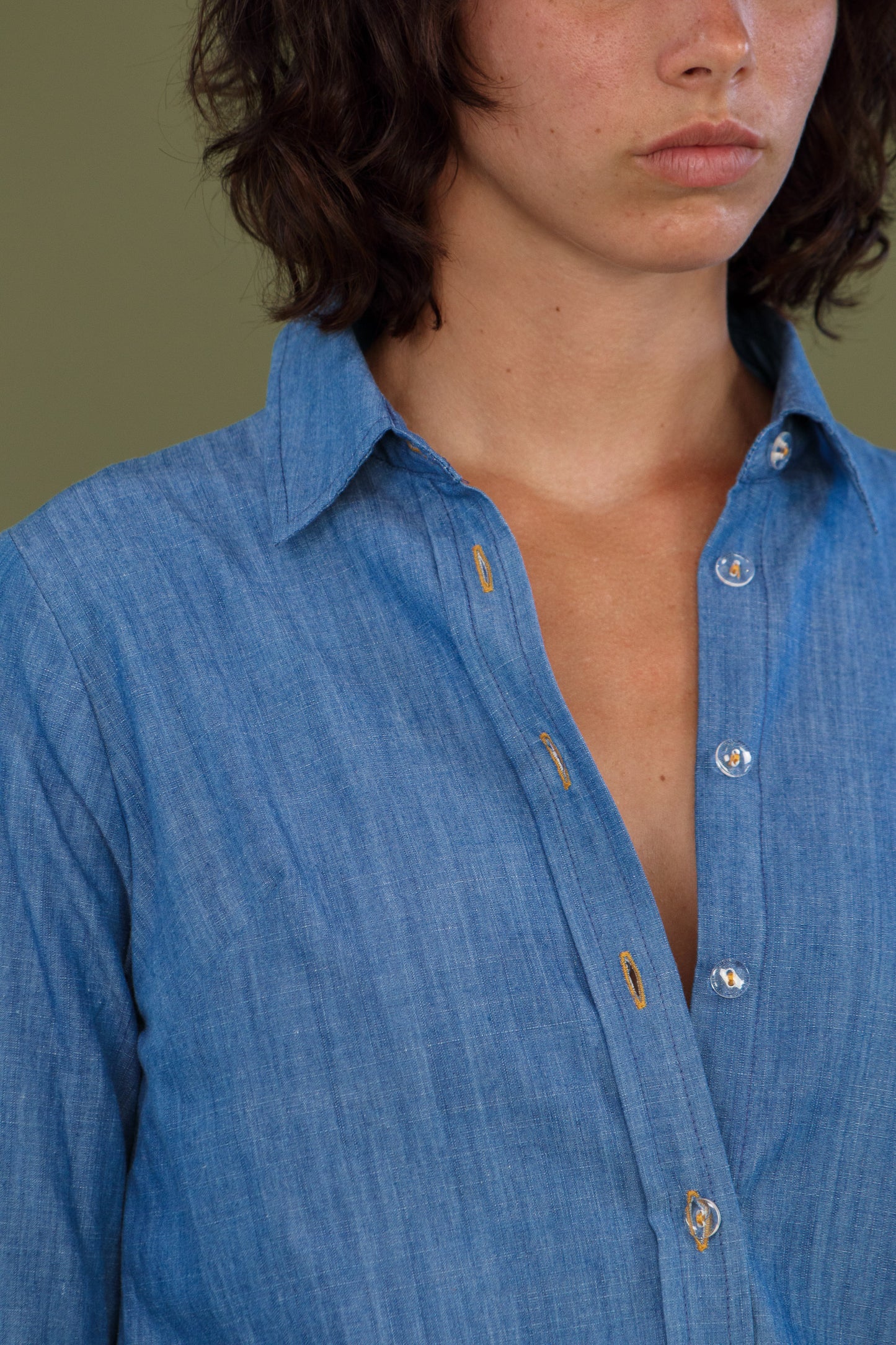 Blue denim shirt worn open showing neckline and contrasting topstitching.