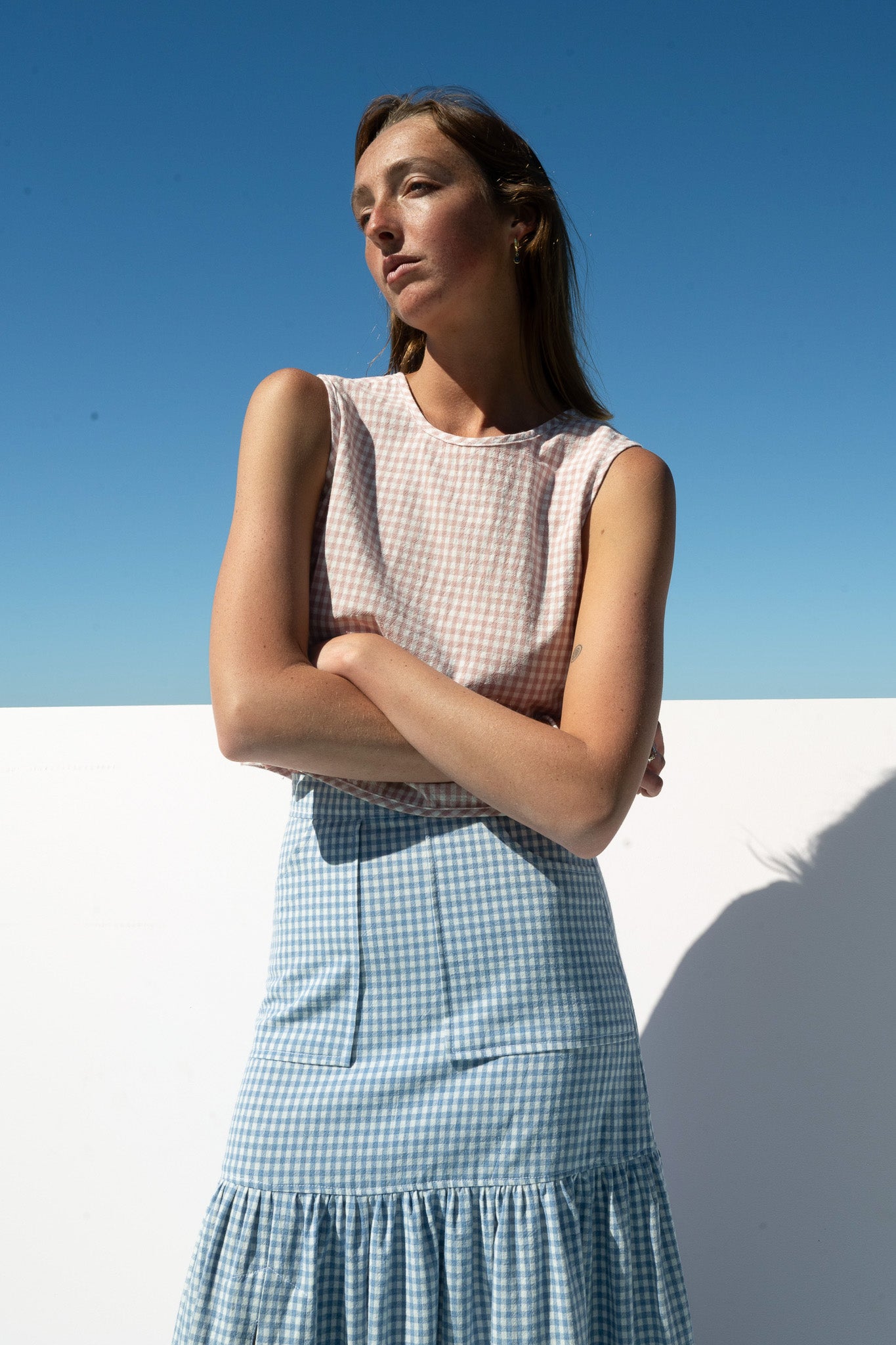 Close-up of The Boy & I Box Crop Top in blush gingham styled with crossed arms and blue cancan gingham skirt