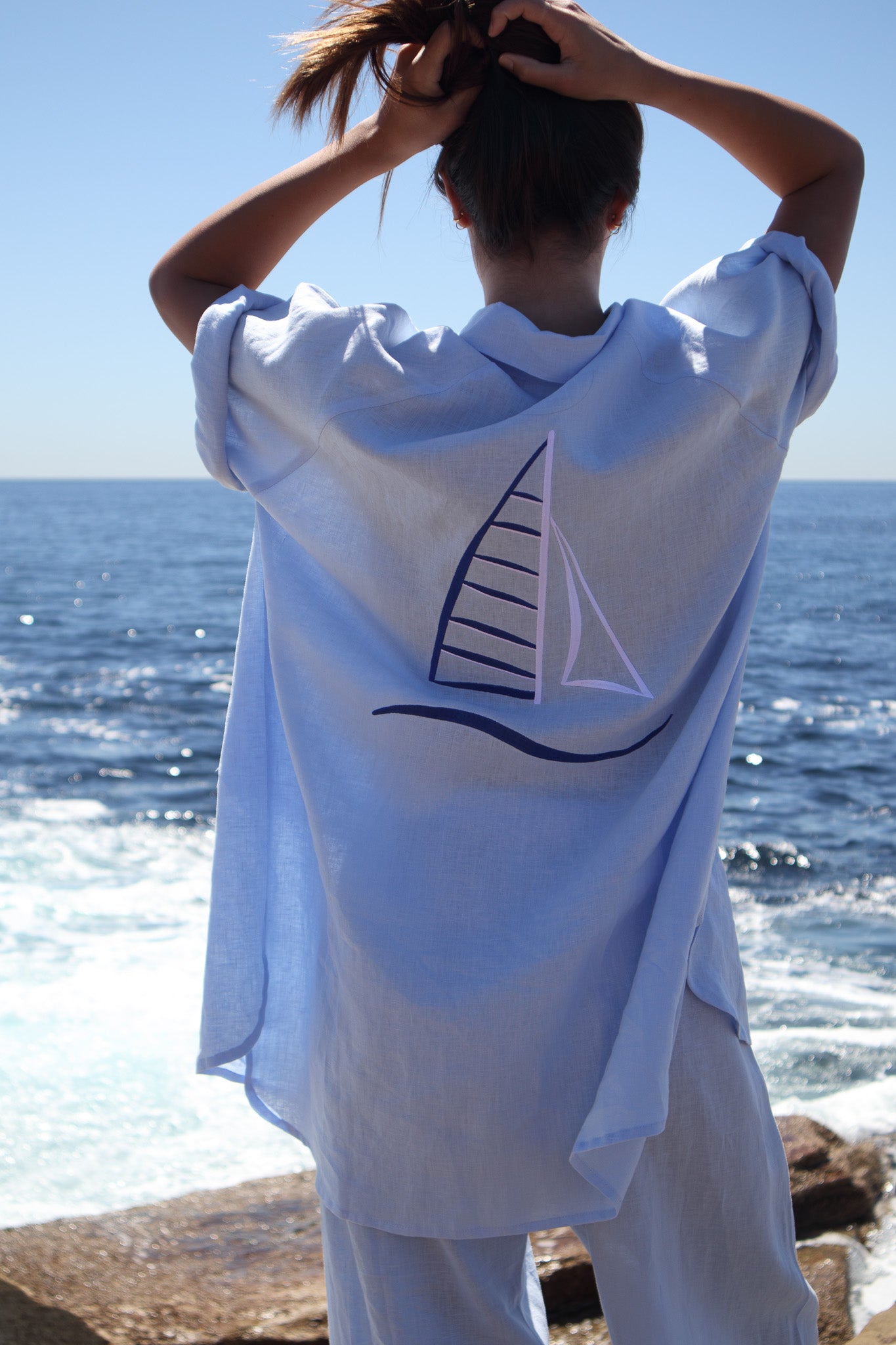Back of the Oceanic Shirt in sail boat with model lifting her hair showing sail embroidery