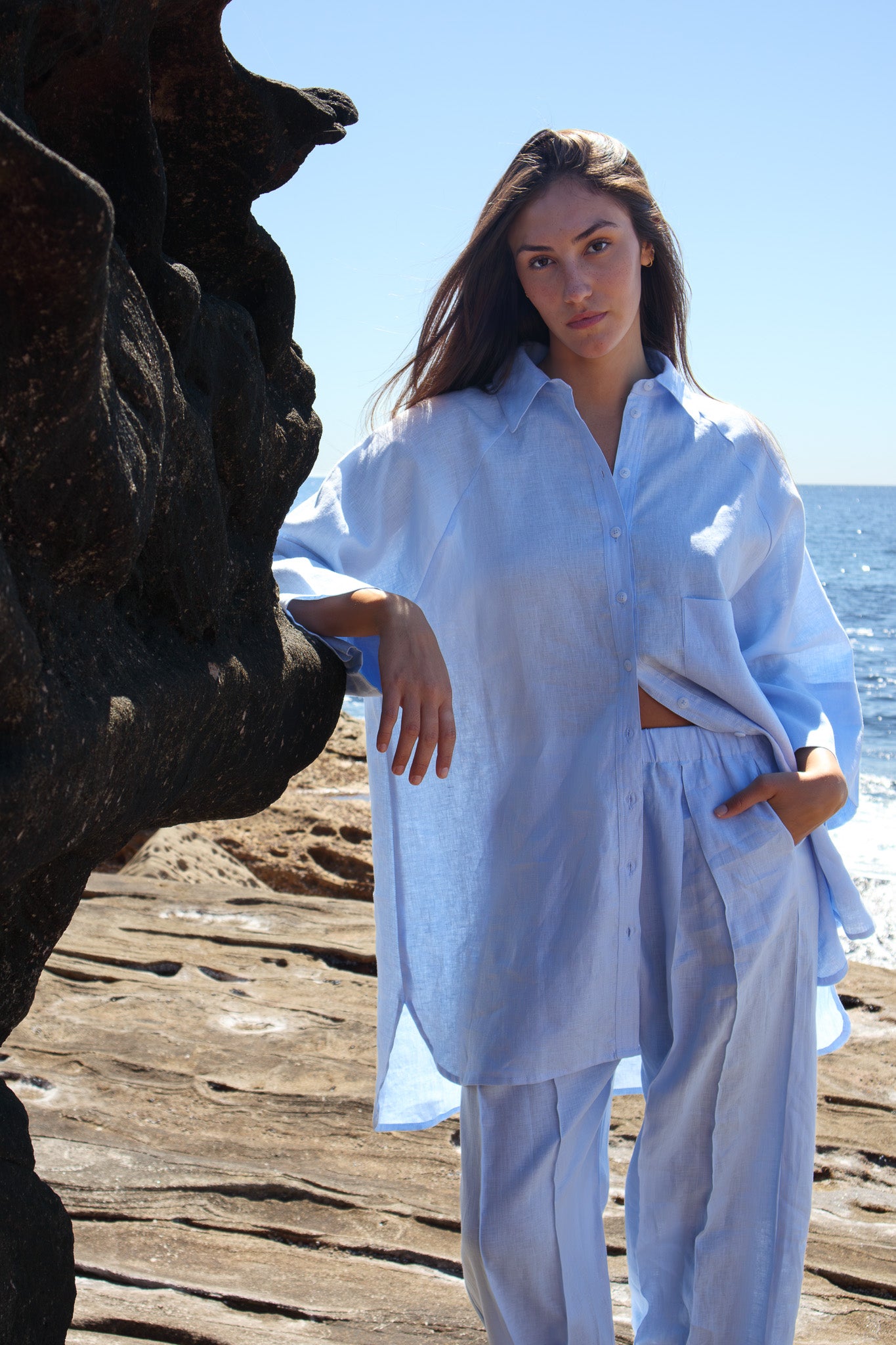 Model wearing the Oceanic Shirt in sail boat standing by coastal rock with ocean behind her