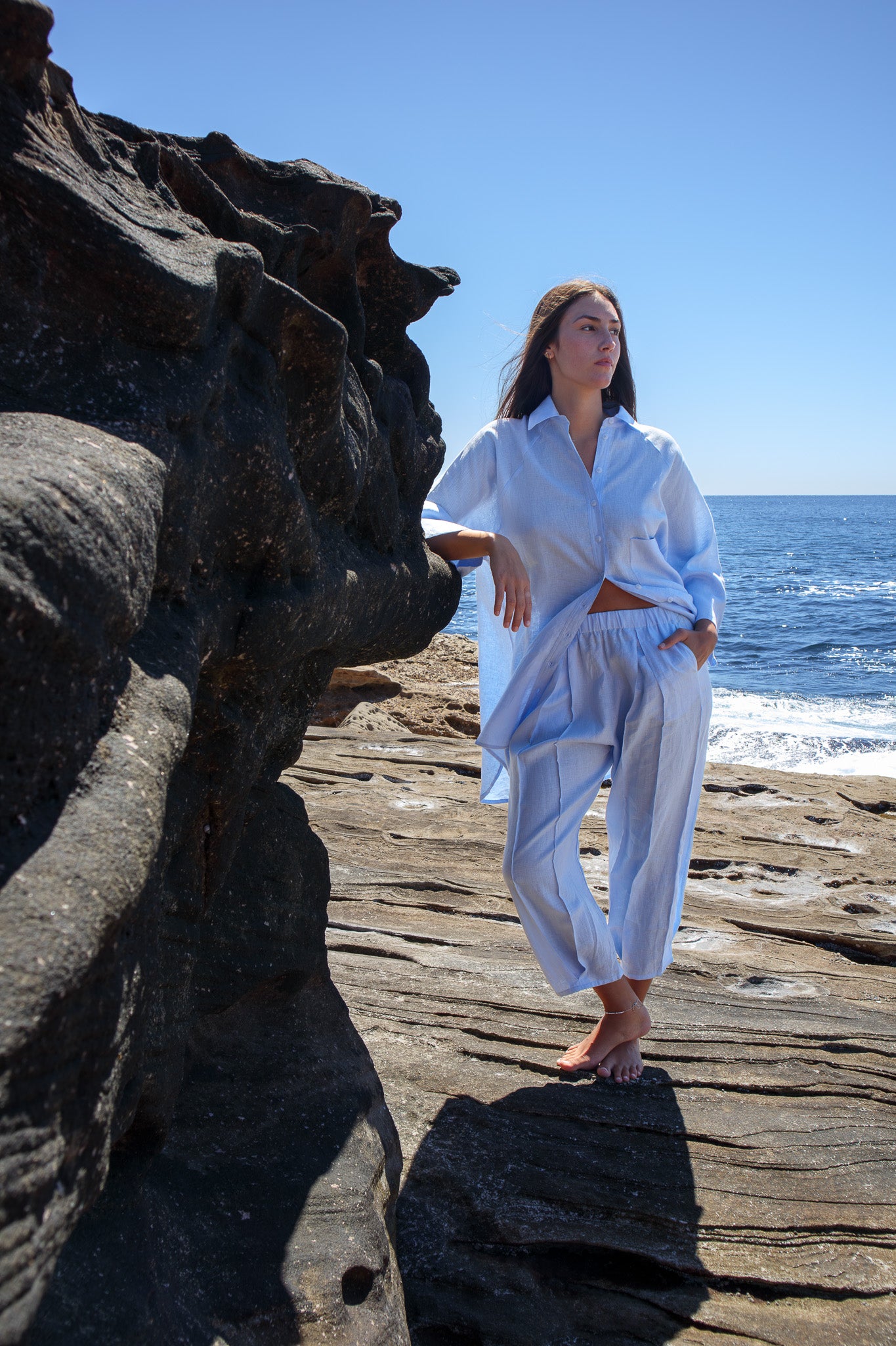 Model wearing the Oceanic Shirt in sail boat with matching pants standing on coastal rock ledge