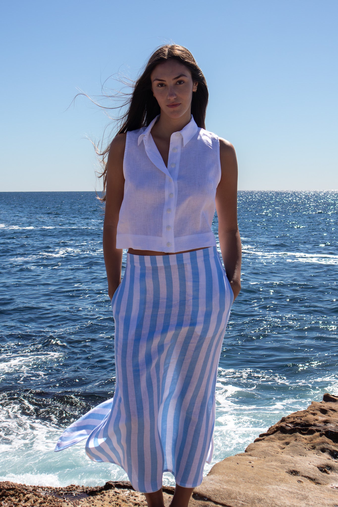 Model wearing the PEPE Top in white French flax linen, styled with the striped skirt, standing by the water under bright summer light.