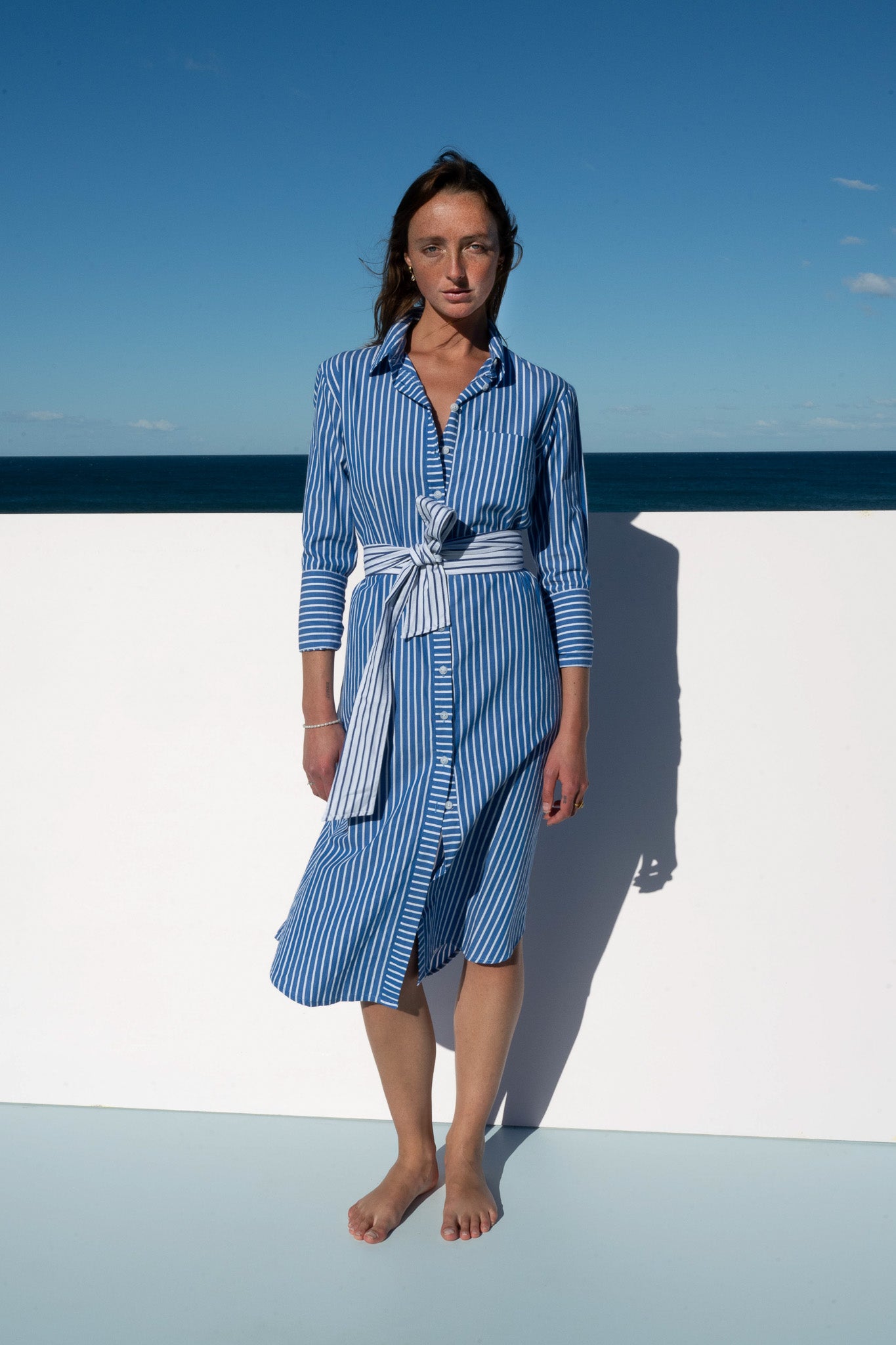 Model wearing the Bronte Dress in blue and white stripe, full-length front view.