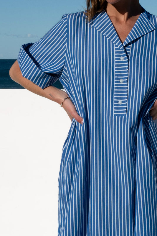 Cabana Dress in blue stripe cotton, close-up front view with model’s hands on hips.