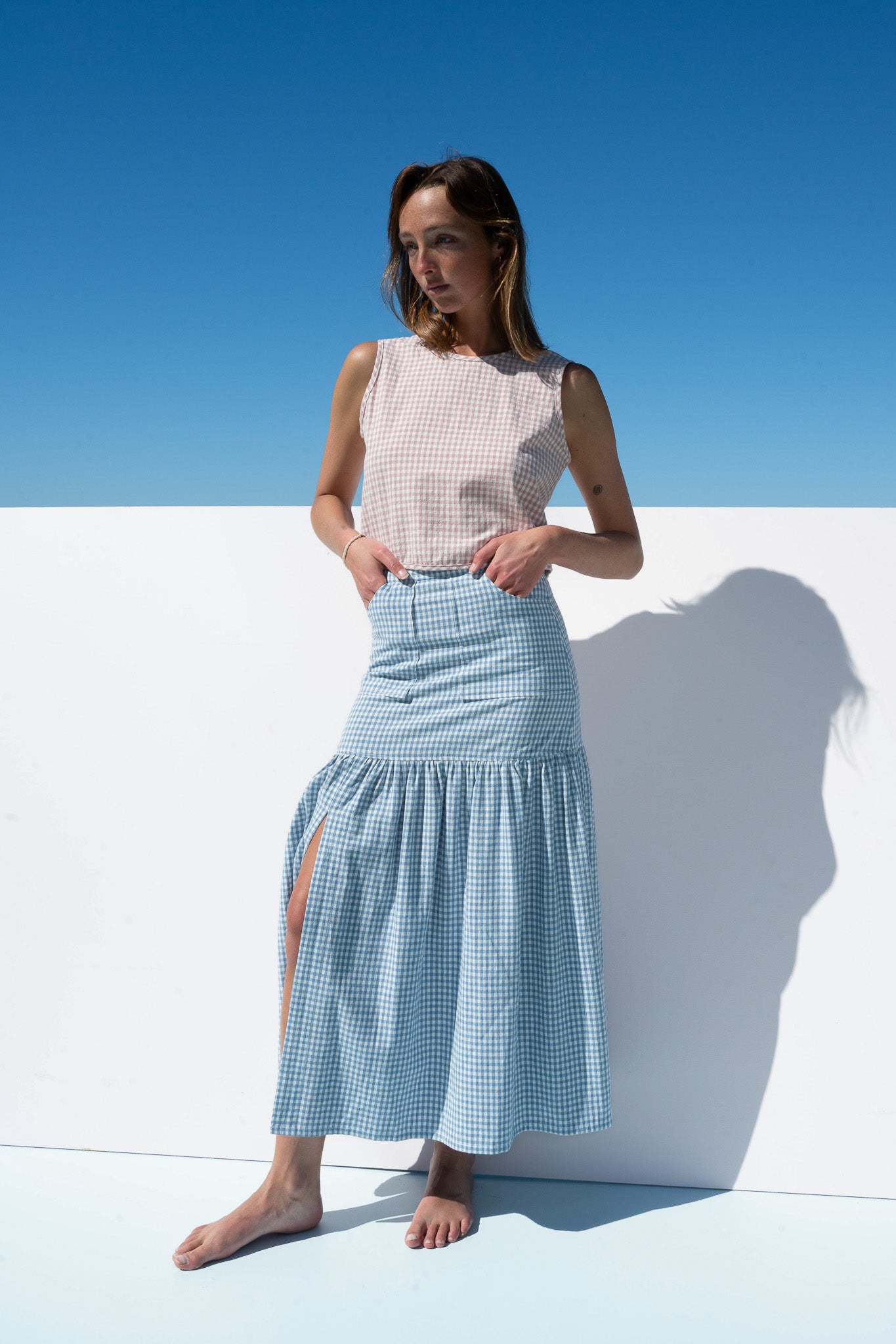 Model wearing Cancan Skirt in blue gingham with blush gingham crop top, photographed front view against ocean backdrop.