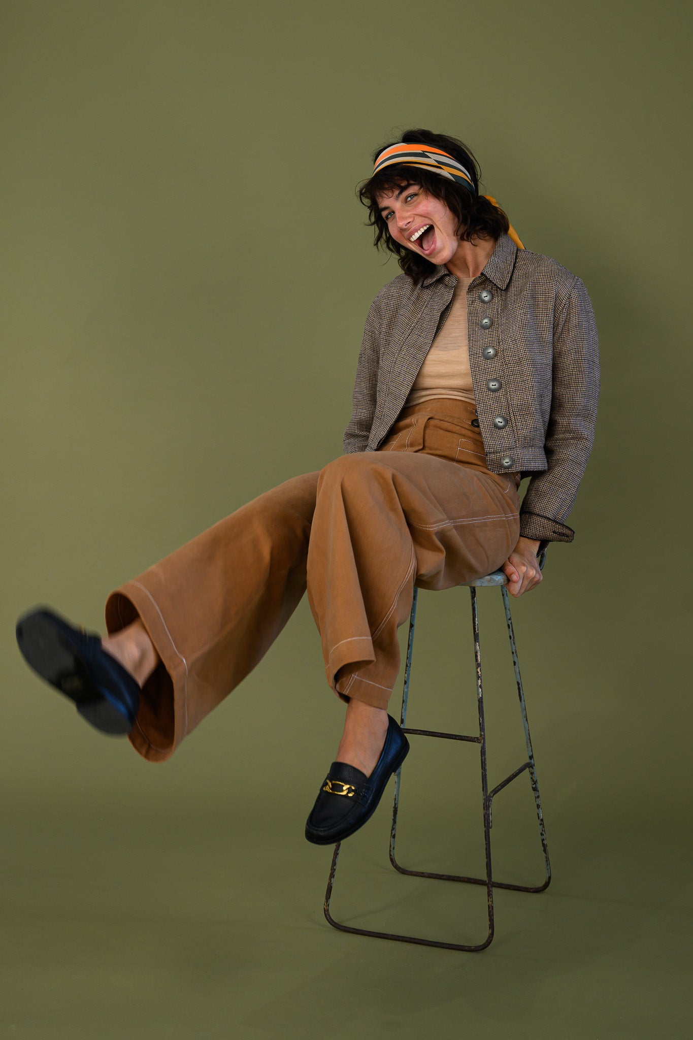 Cropped check jacket styled outfit with relaxed pants shown seated on stool
