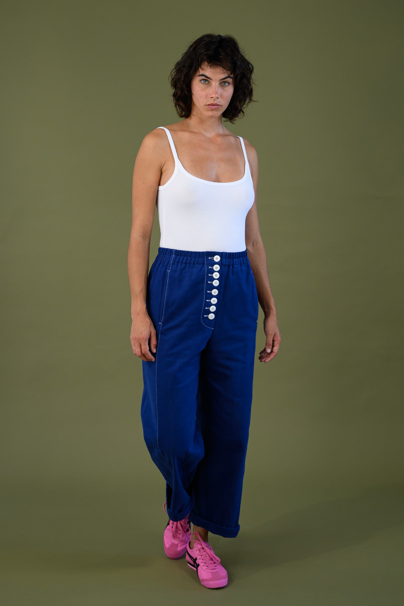 Front walking view of French navy cotton twill button pants showing high waist and front button detail styled with white tank