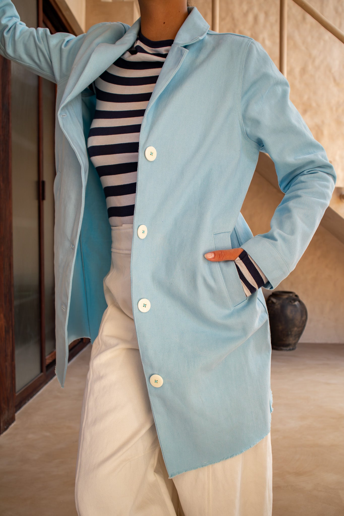 Close-up of front buttons and pocket of the Hunter Coat in Light Sky Blue cotton twill suede, styled with a striped top.