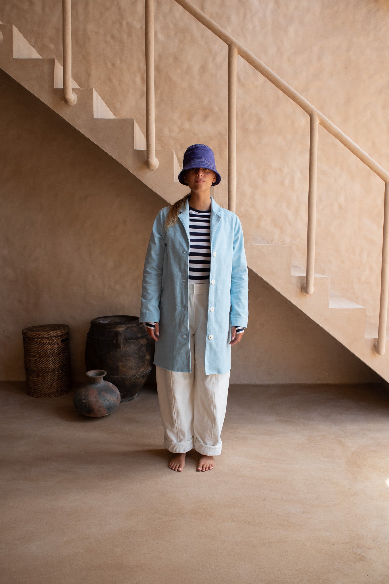 Front view of the Hunter Coat in Light Sky Blue cotton twill suede with white buttons, paired with striped tee.