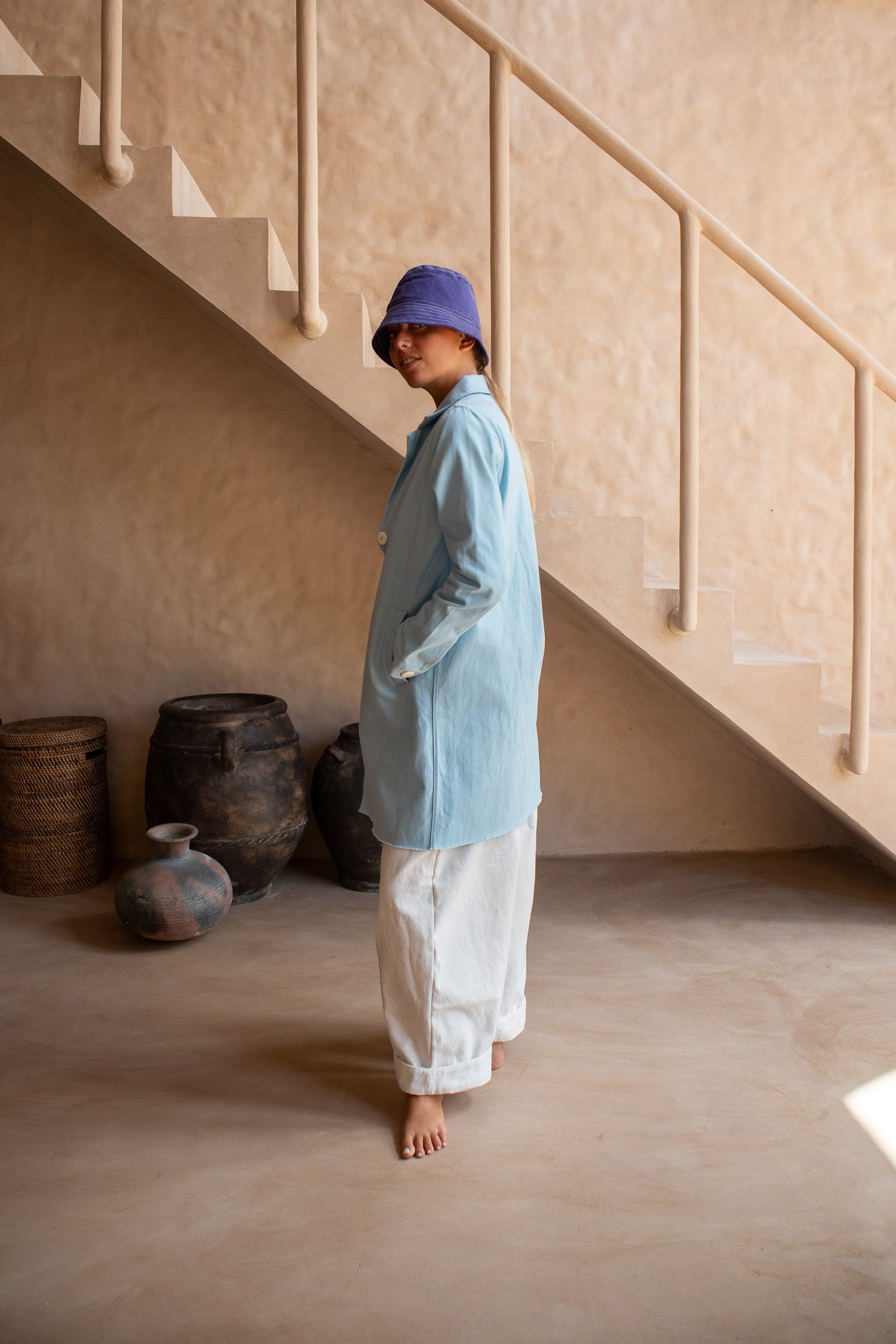 Side profile of the Hunter Coat in Light Sky Blue cotton twill suede, styled with white pants and a bucket hat.