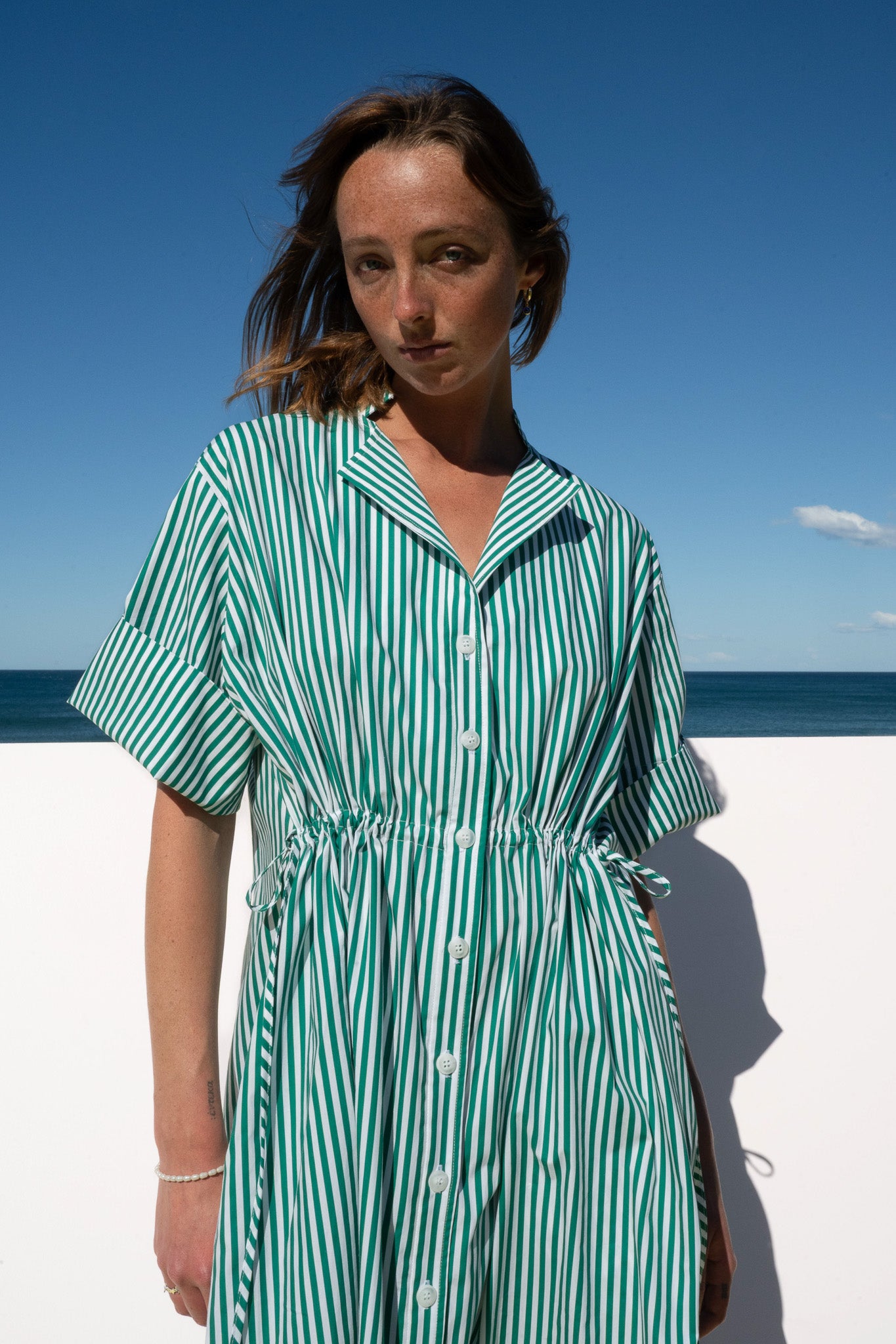 Portrait view of the Leon Dress in lush green meadow stripe, featuring classic collar, white buttons, and gathered waist detail.