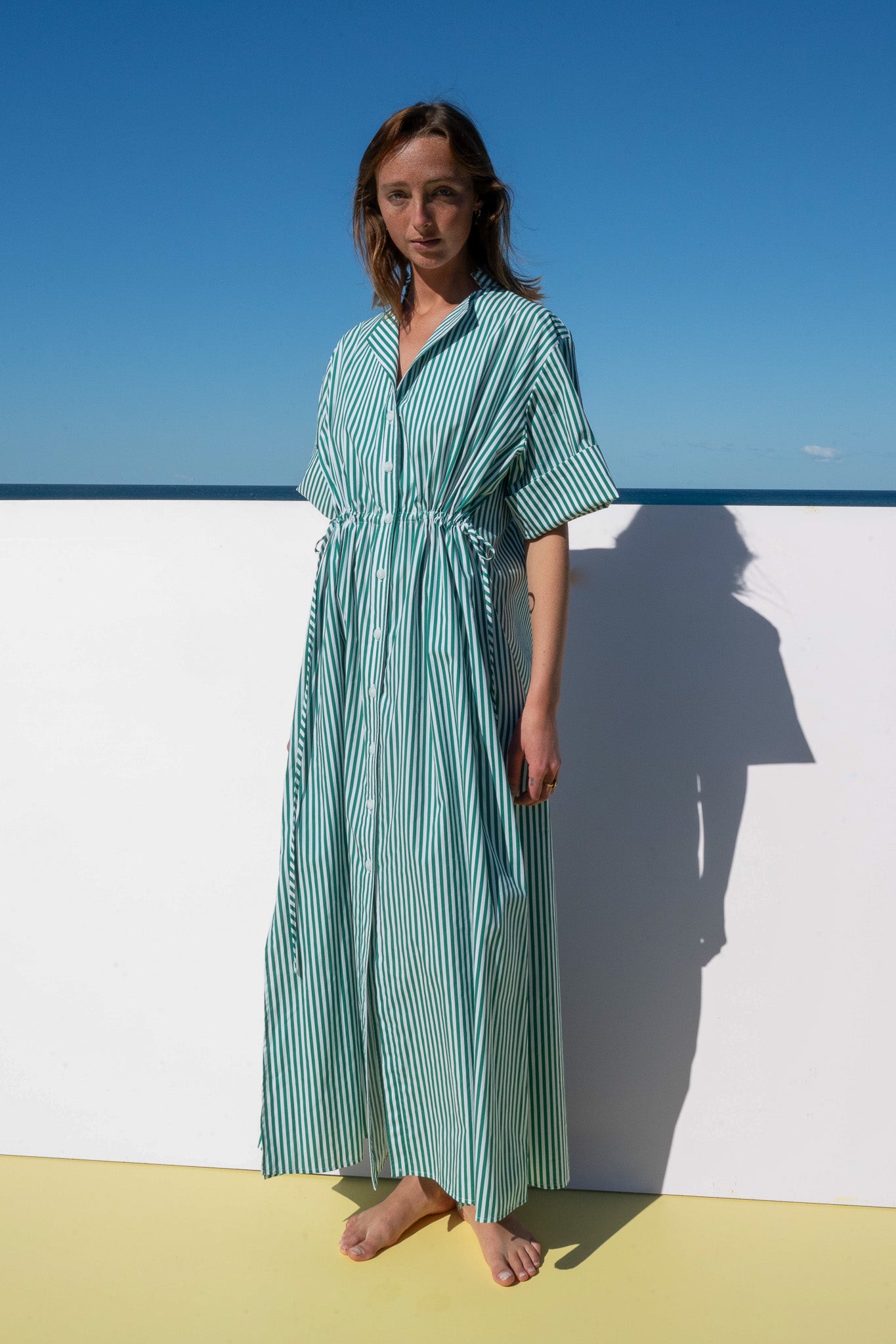 Full length view of the Leon Dress in lush green meadow stripe, a button-down style with relaxed shape and cinched waist.