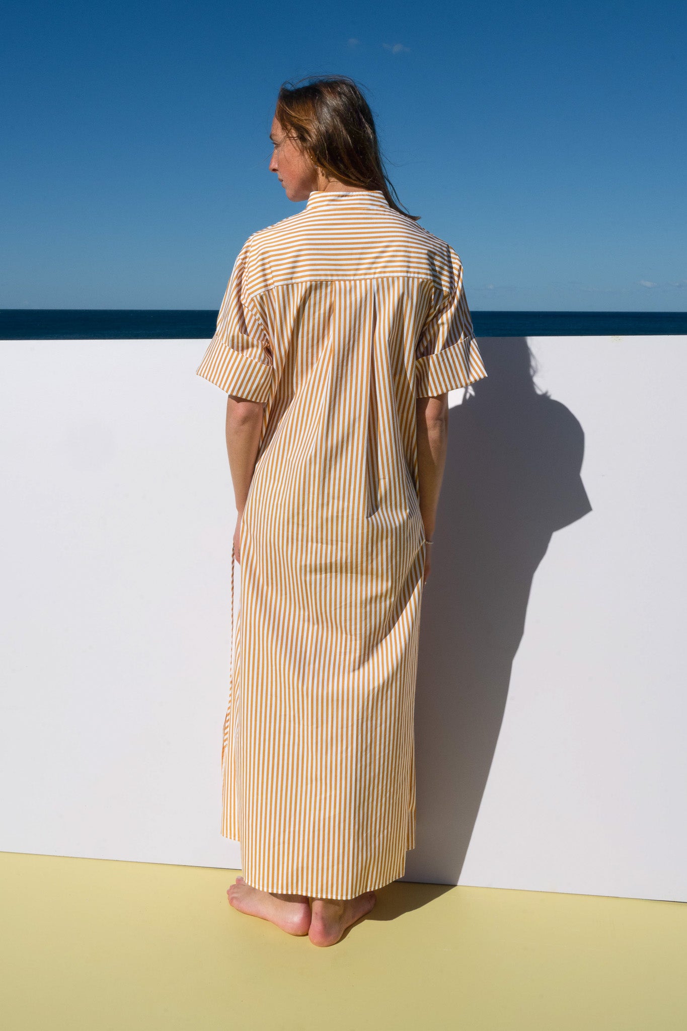 Back view of the Leon Dress in marigold stripe highlighting longline silhouette and vertical stripes.