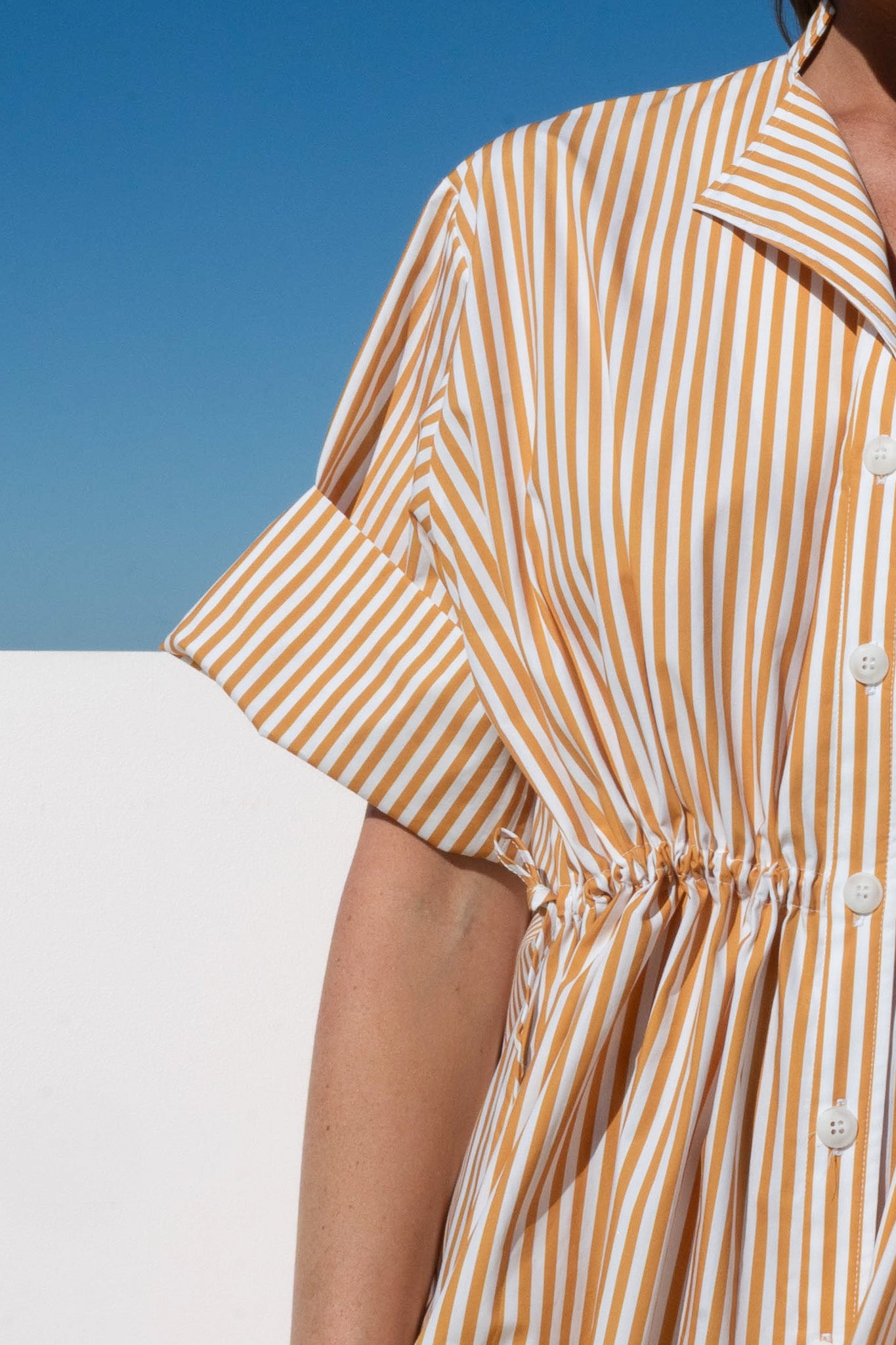 Close-up of the Leon Dress in marigold stripe showing short cuffed sleeve and drawstring waist detail.