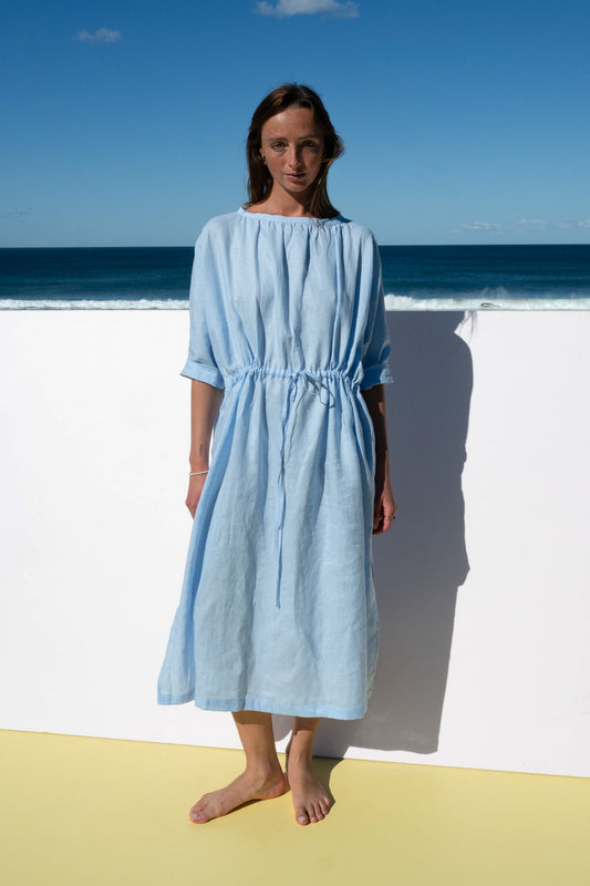 Front view of The Moments Dress in corn flour blue linen, with gathered waist and relaxed sleeves.
