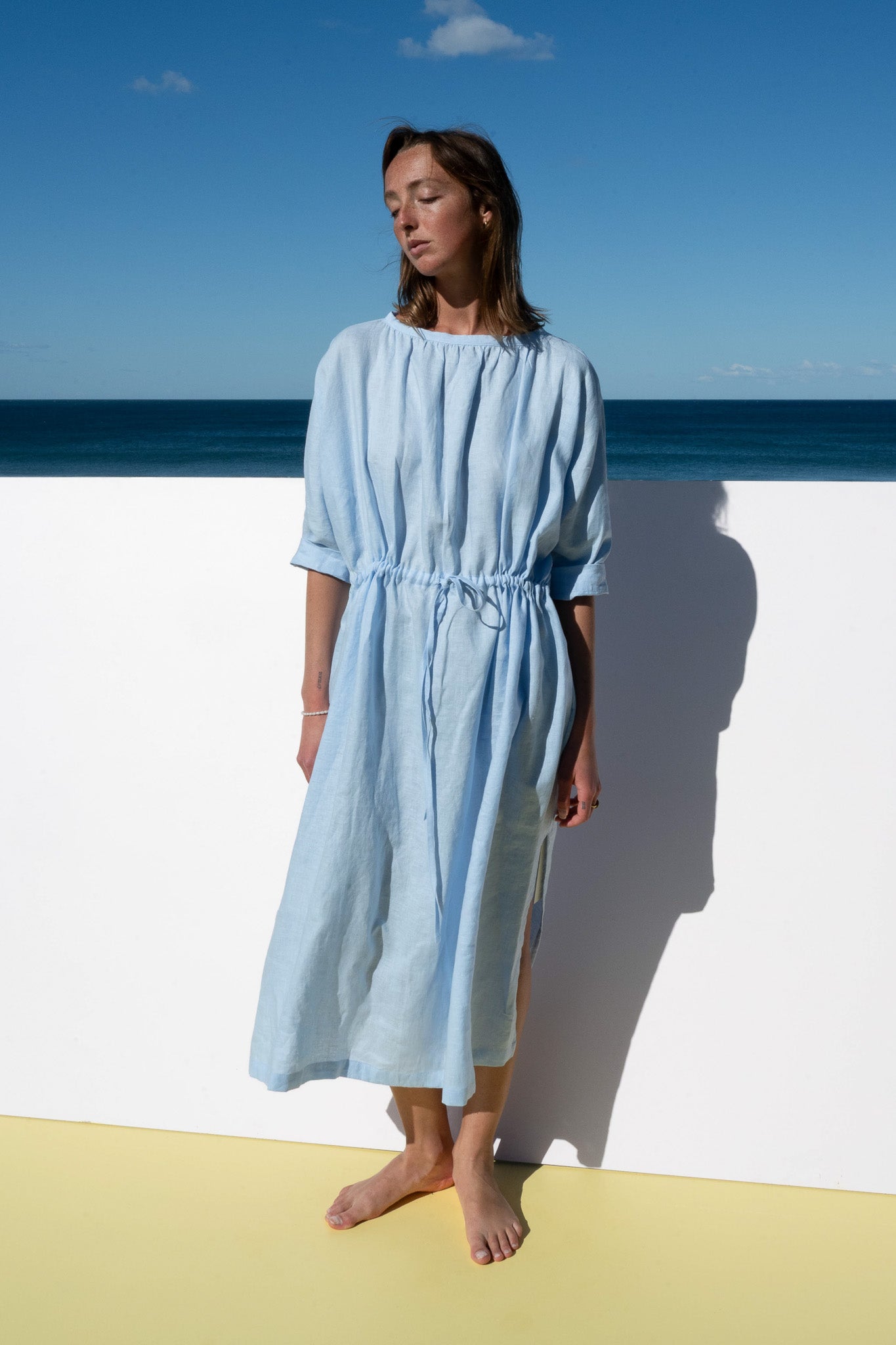 Model wearing The Moments Dress in corn flour blue linen, standing front-facing in soft natural light.