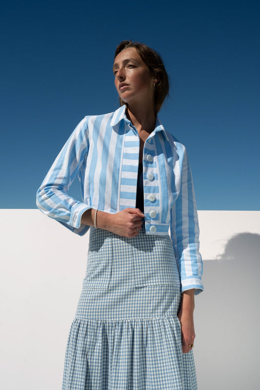 Side-angle view of Mon Petit Jacket Saltwater Stripe with gingham skirt, ocean in the background.