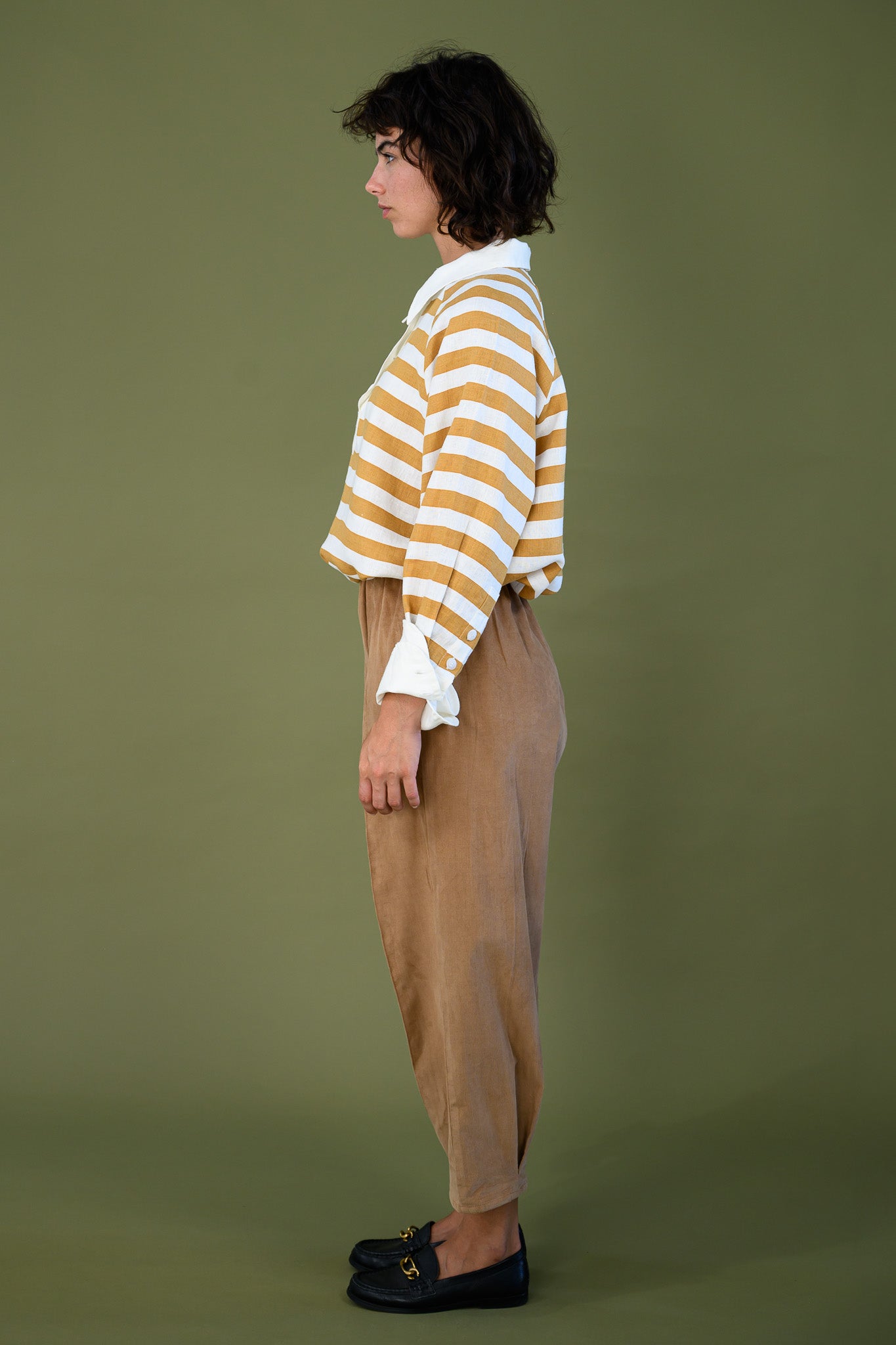 Salt pant in tawny brown cotton corduroy worn side profile with striped top showing relaxed fit and tapered leg