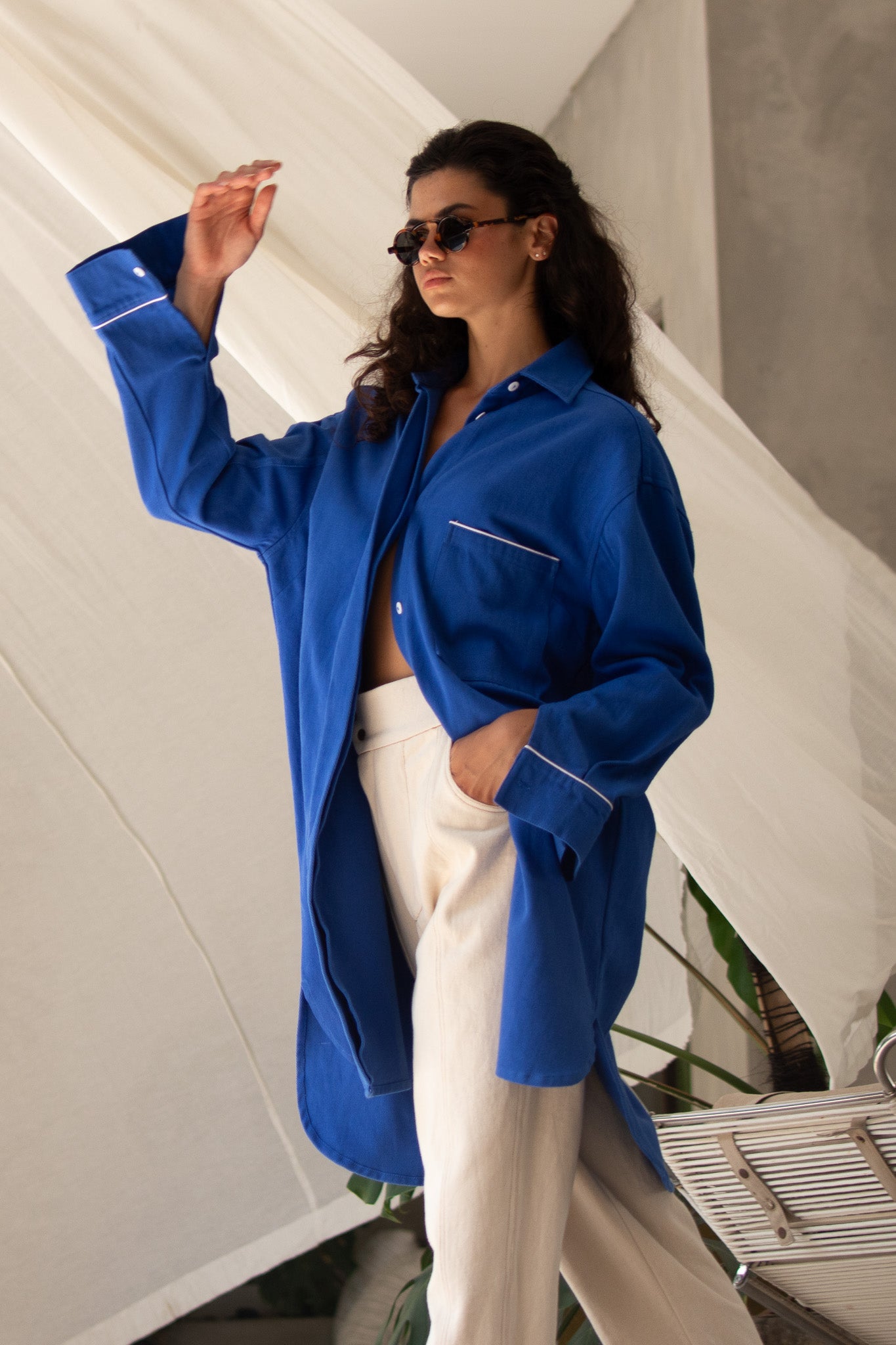 Moody shot of model wearing denim blue jacket with curtain blowing in the background