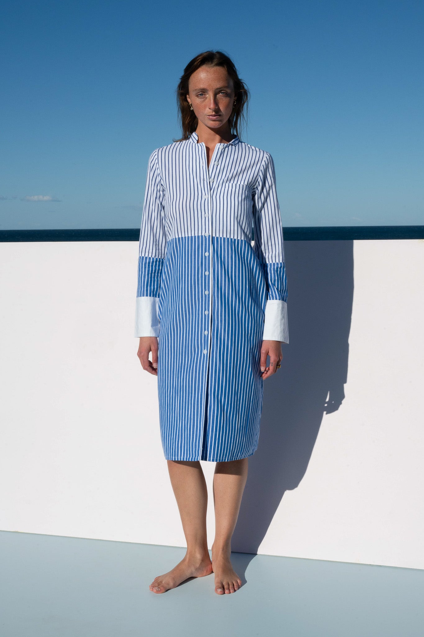 Model wearing the Sisto Dress in blue and white stripe, buttoned front view.