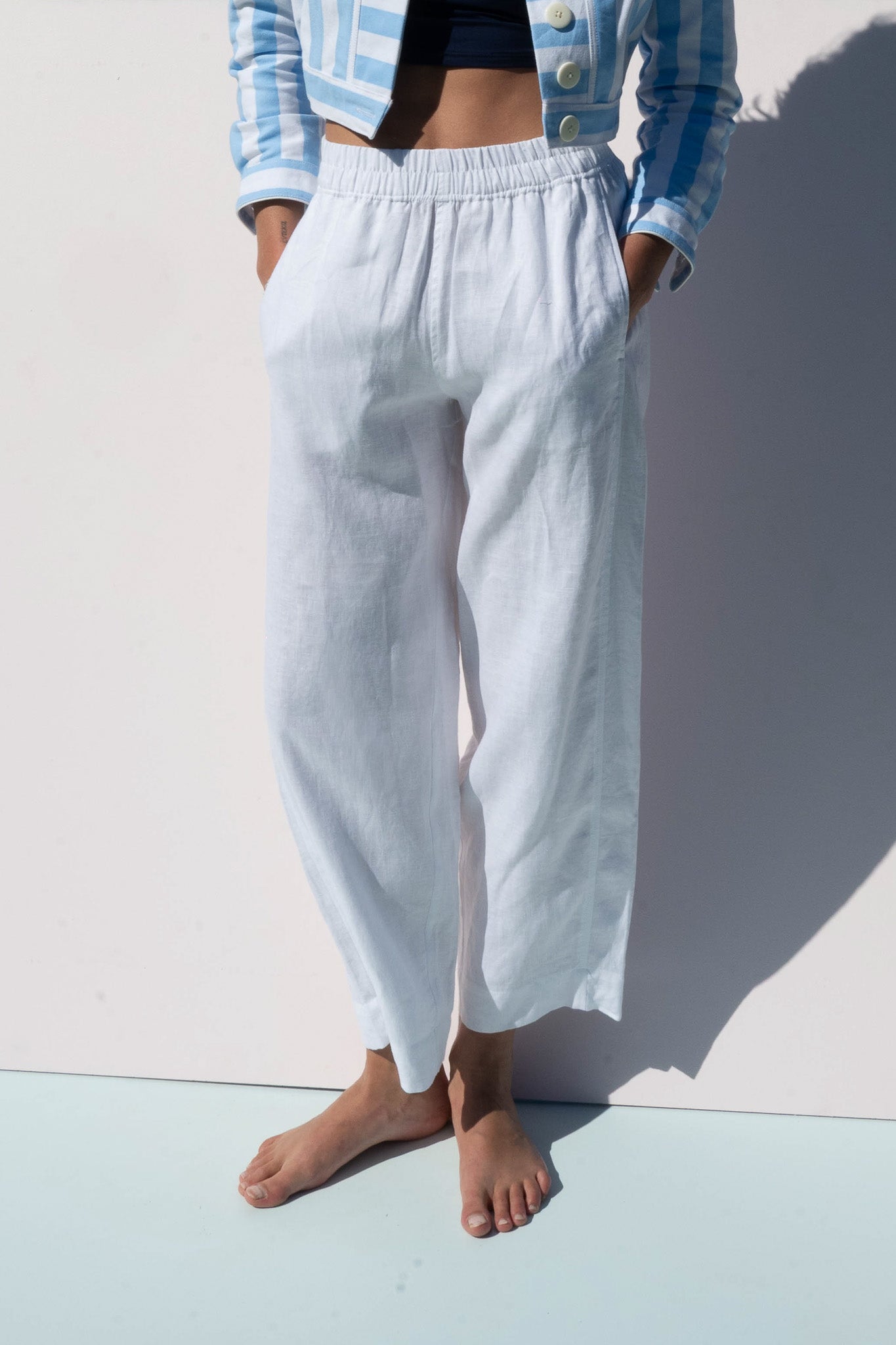 Close-up of Solero Pant in white linen, showing relaxed fit and pockets, paired with a blue striped cropped jacket.