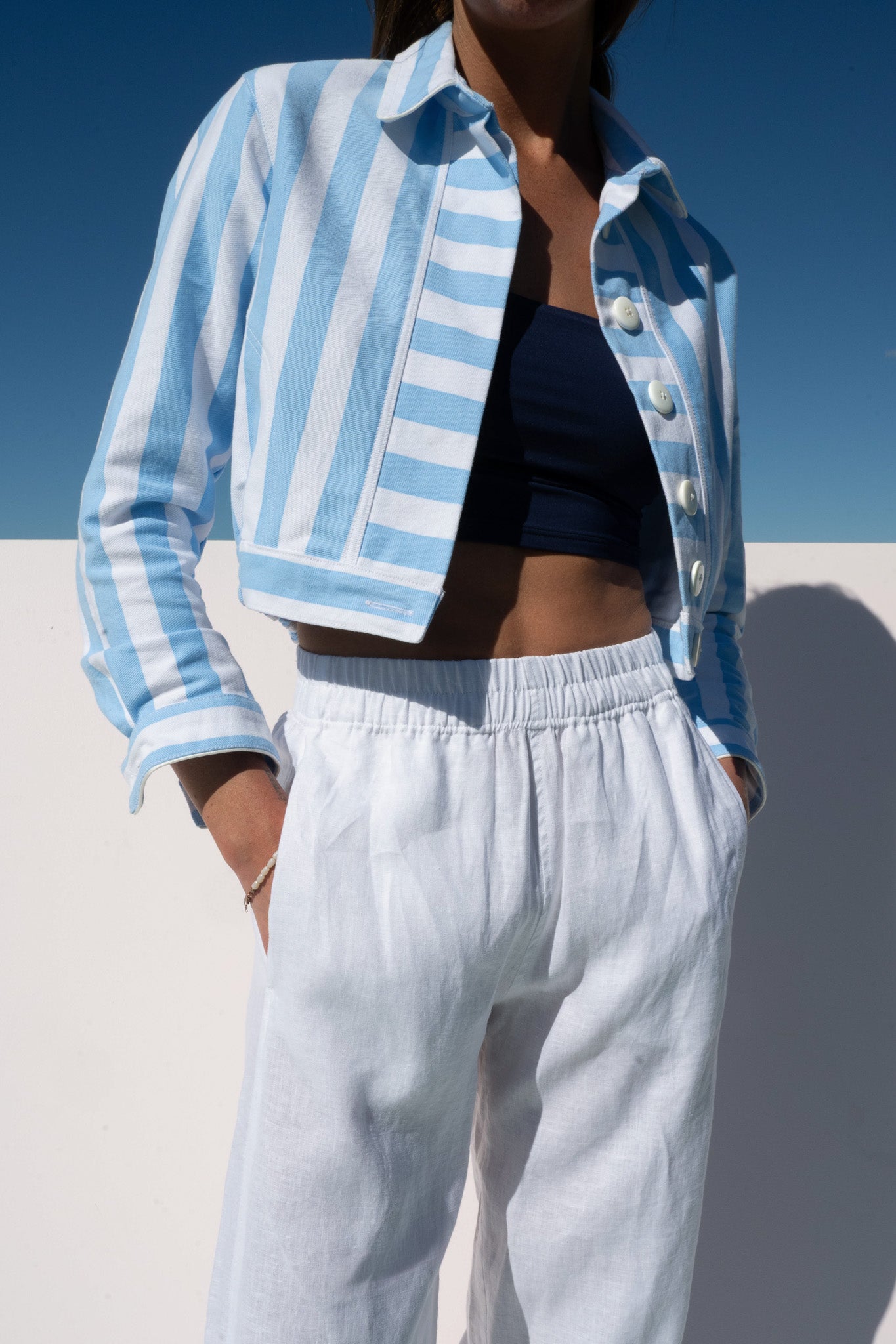 Side detail of the Solero Pant in white linen with elastic waistband, styled with a cropped blue striped jacket.