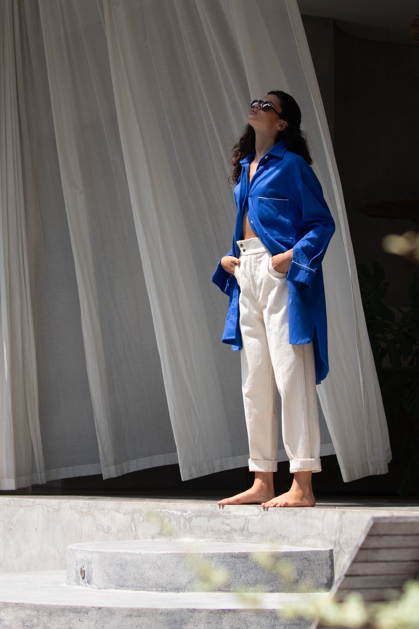 model looking up at the sky with curtain in the background blowing in the wind, wearing denim blue jacket and raw denim pant